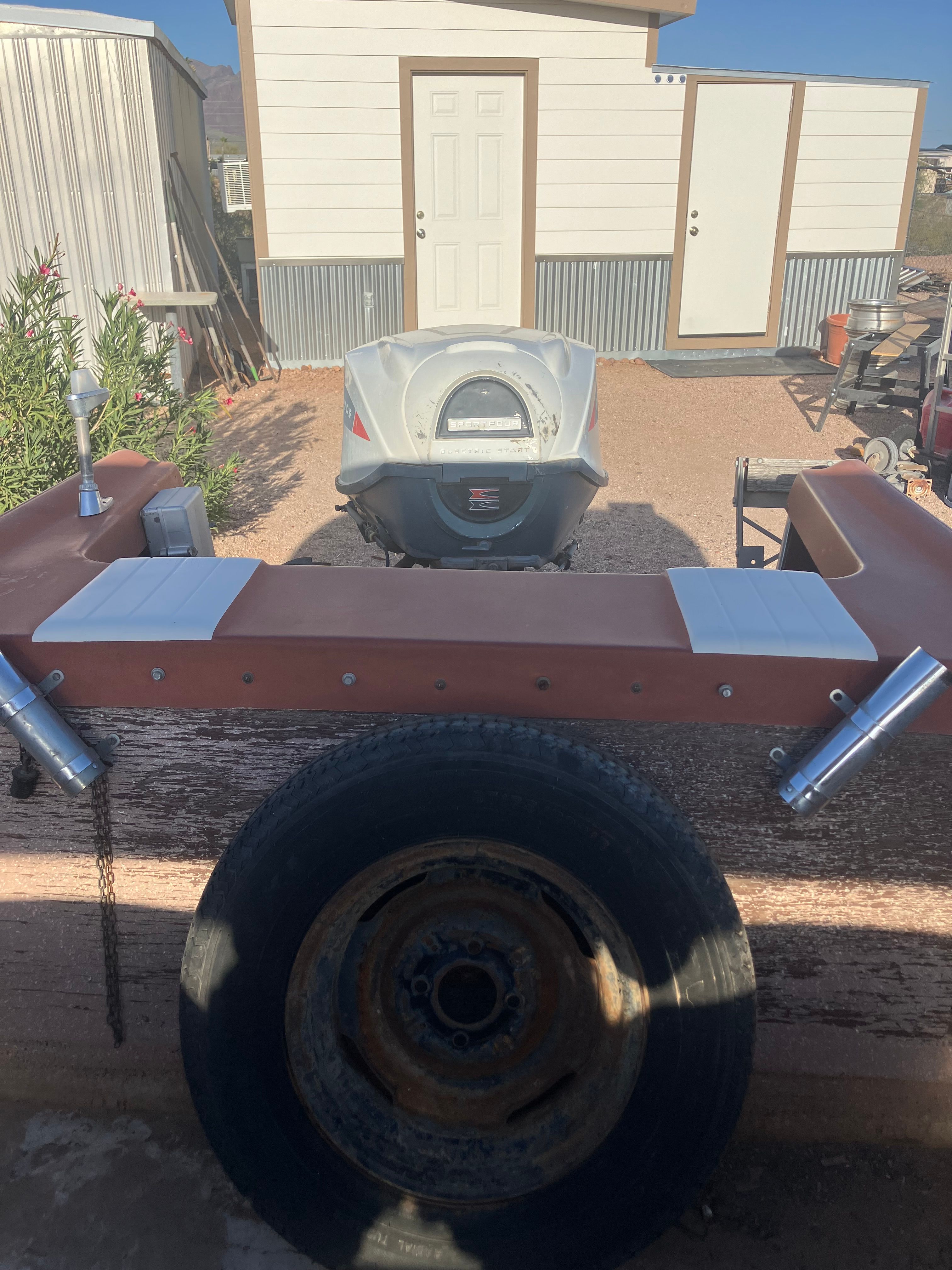 A 1958 Hydroswift Runabout with an outboard motor on a trailer, parked in front of a building.