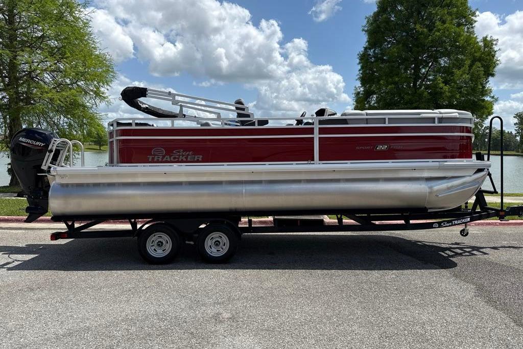 2026 Sun Tracker SportFish 22 DLX pontoon boat on trailer, parked near a lake.