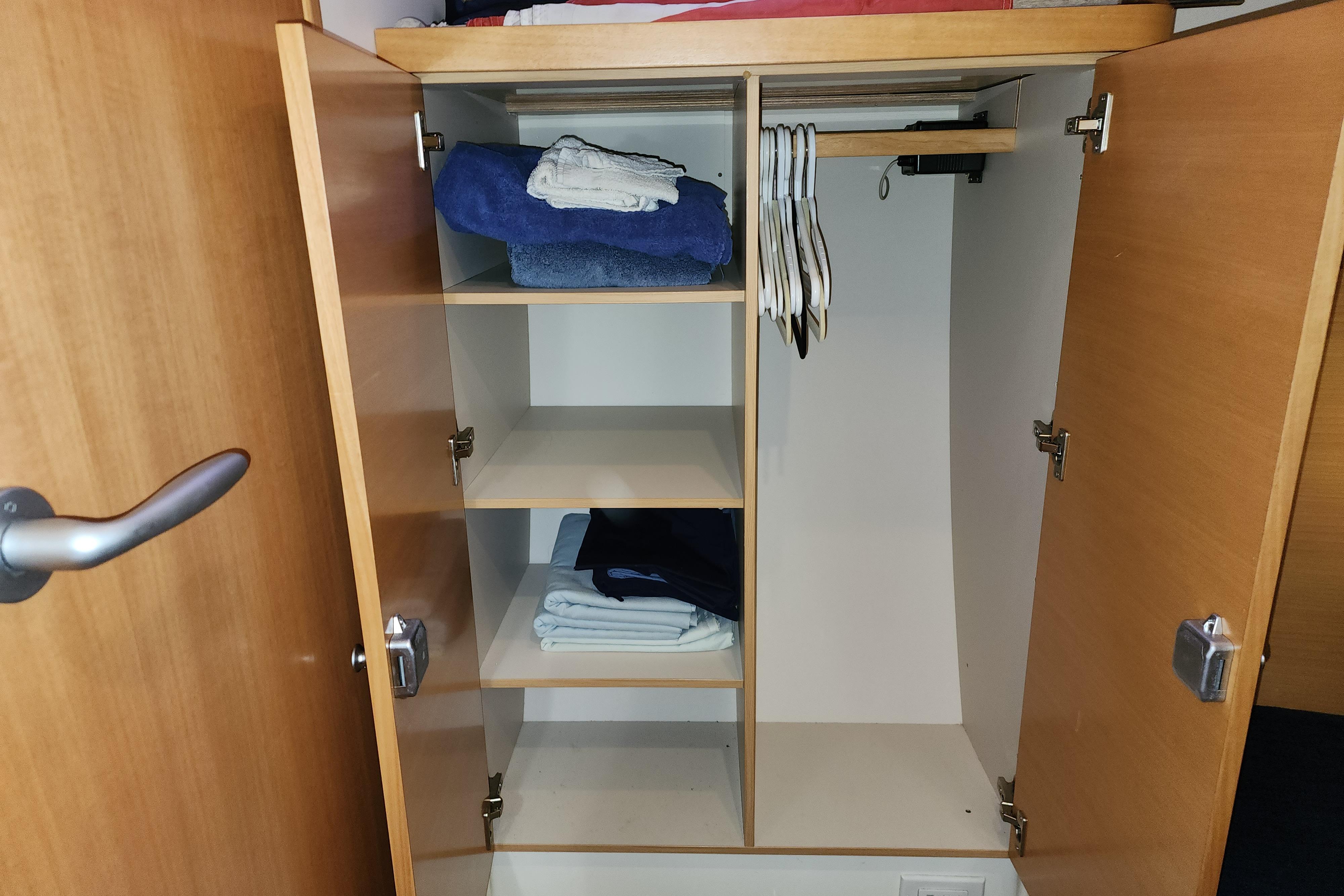 Open wooden closet with shelves, hangers, and folded clothes on a 2007 Hanse 400e.