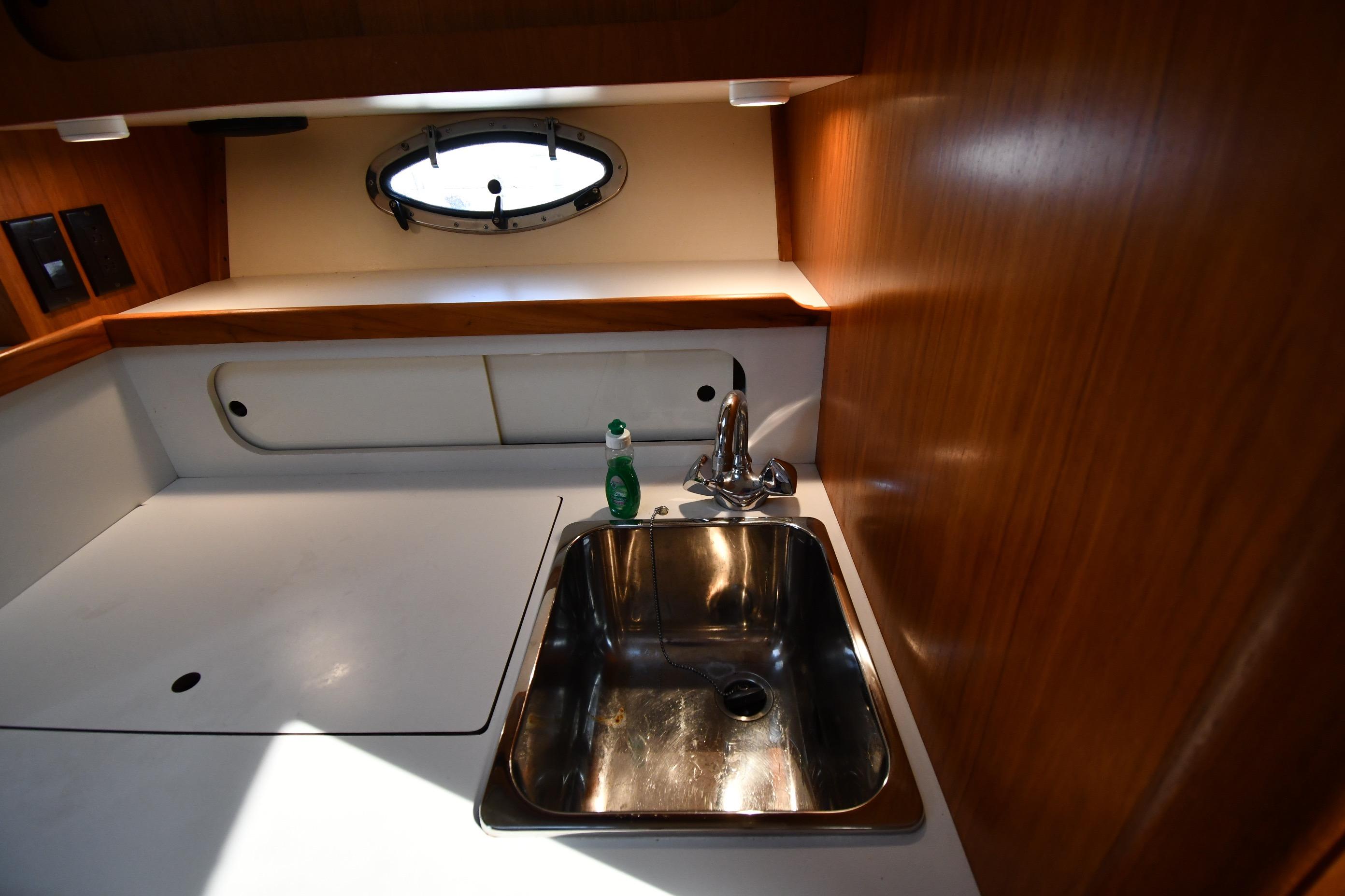 1998 Tiara Yachts 3100 Open galley with sink, wooden cabinetry, and porthole window.