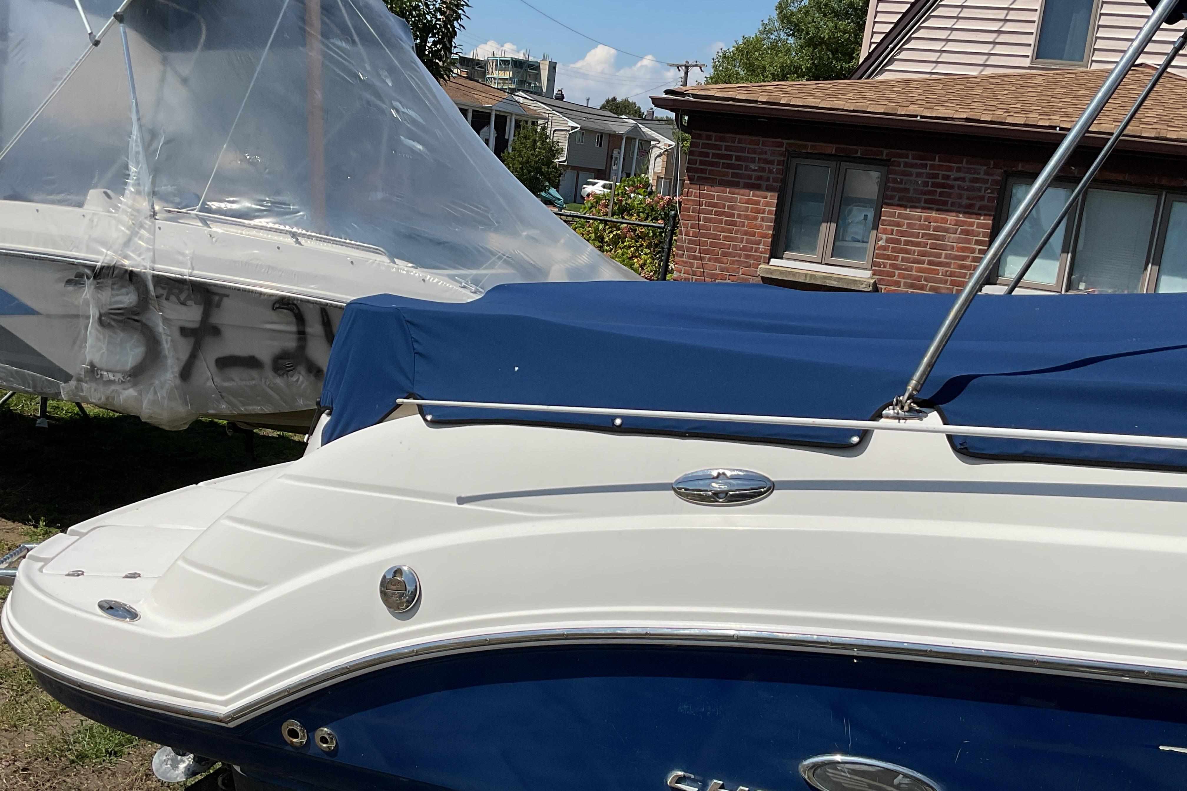 2006 Chaparral 256 SSi boat with blue cover, parked near a brick house.