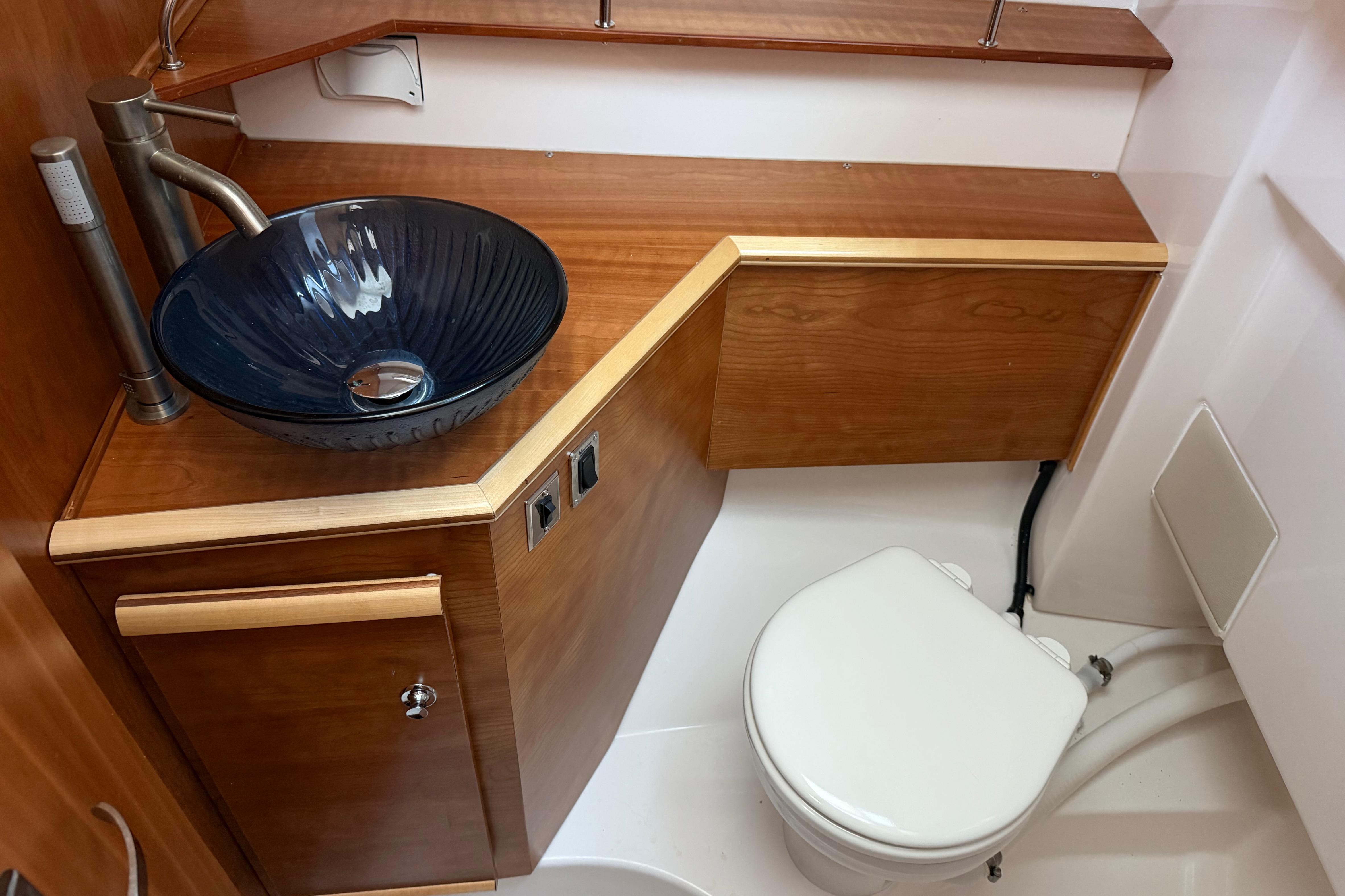 2023 Cutwater C-288 Coupe bathroom with wooden cabinetry and modern glass sink.