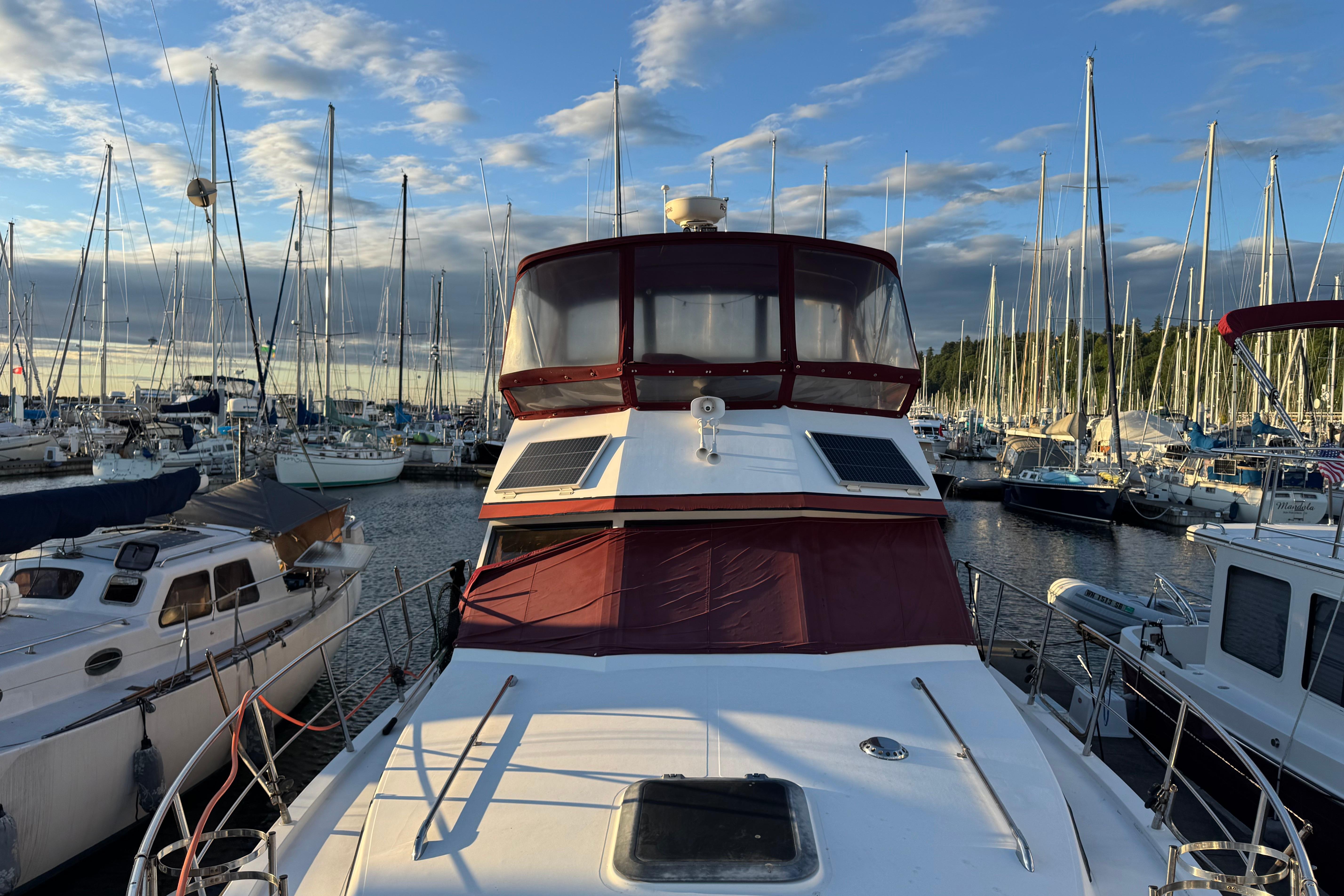1987 President 37 yacht docked in a marina, surrounded by sailboats under a blue sky.