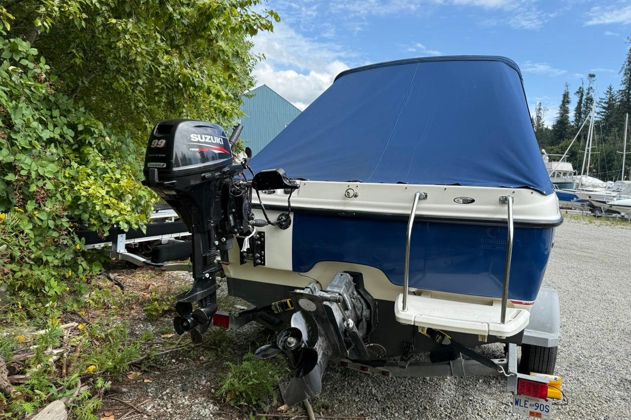 2005 Bayliner 210 Discovery boat with Suzuki outboard motor, covered and parked outdoors.
