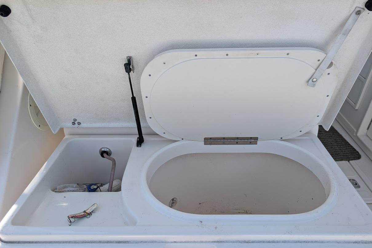 Open storage compartment on a 2000 Pursuit 3400 Express boat, featuring a sink and fishing lure.
