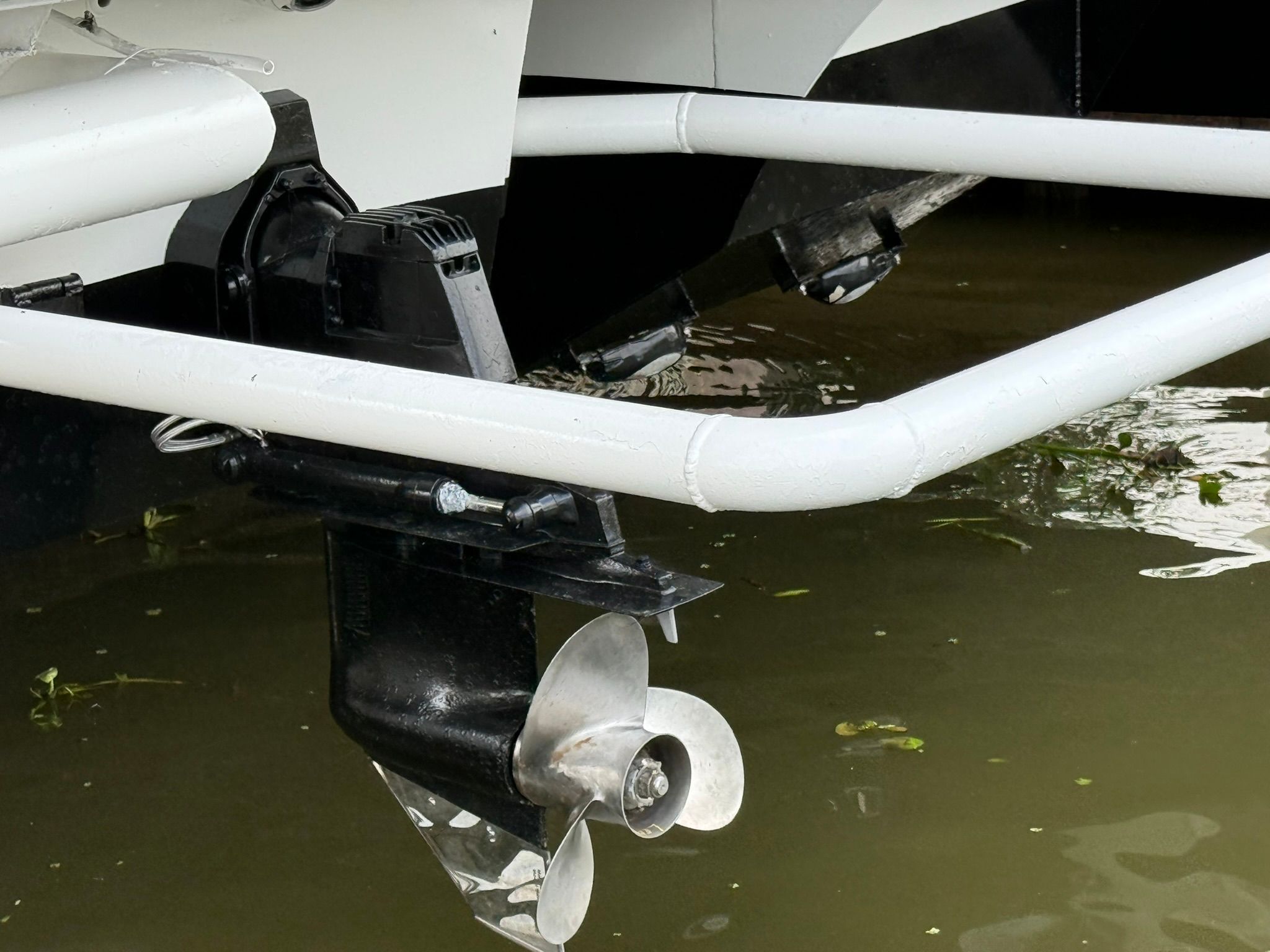 Close-up of a boat propeller in water, surrounded by white pipes.