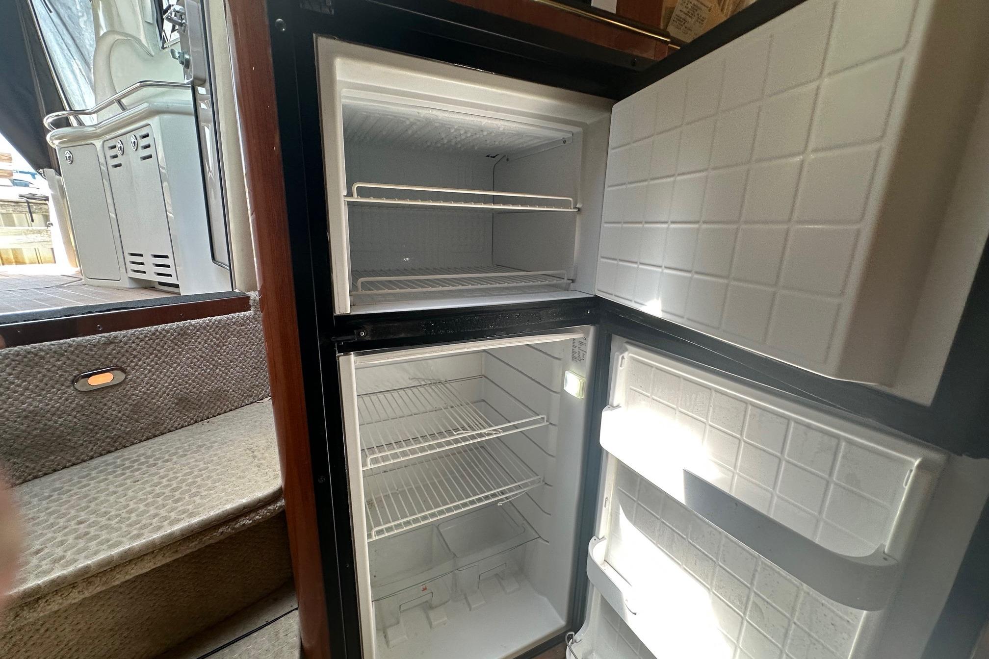 Open refrigerator inside 2001 Sea Ray 410 Sundancer yacht, showing empty shelves and steps nearby.