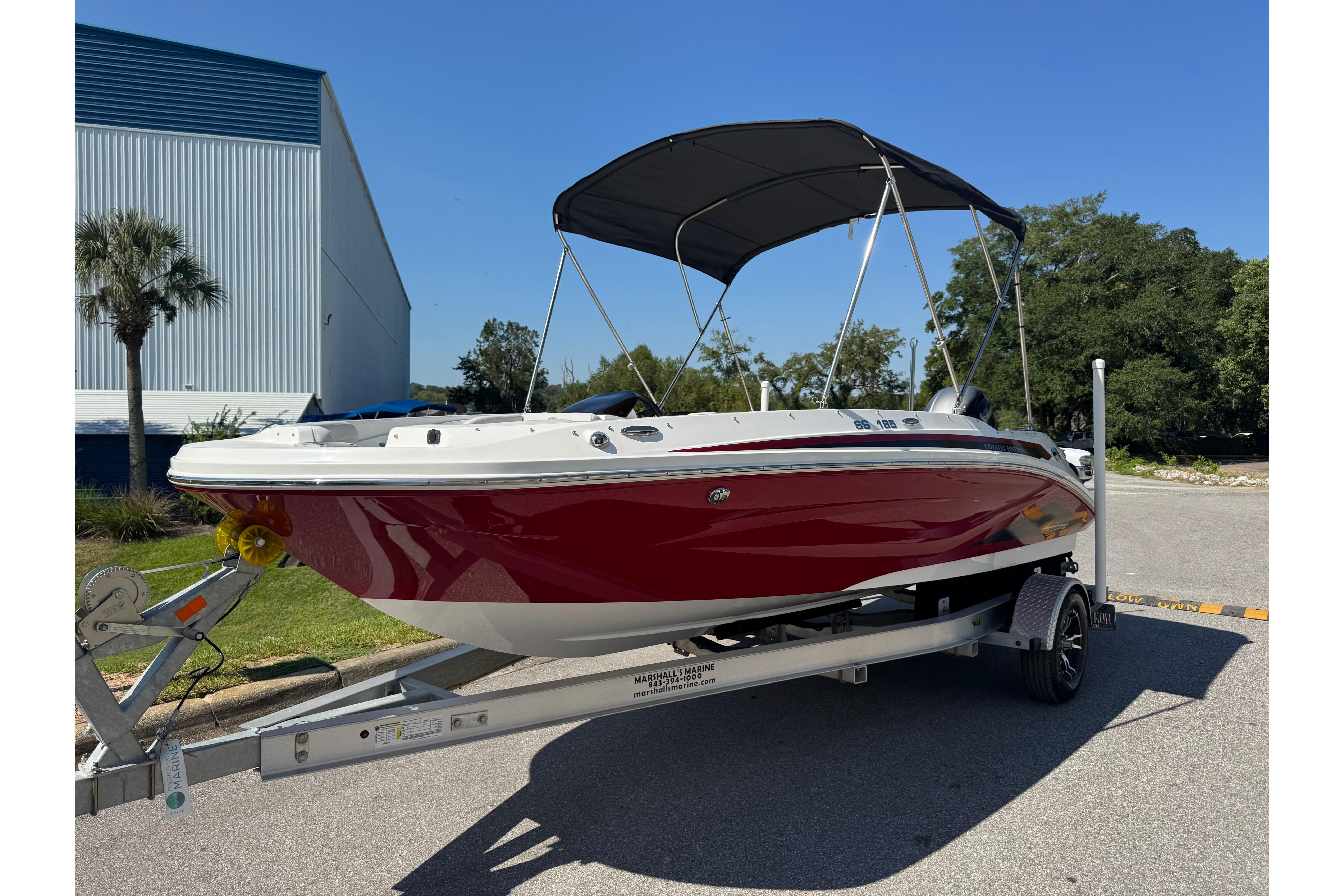 2021 Hurricane SunDeck Sport 185 OB boat on trailer, red hull, black canopy, outdoor setting.