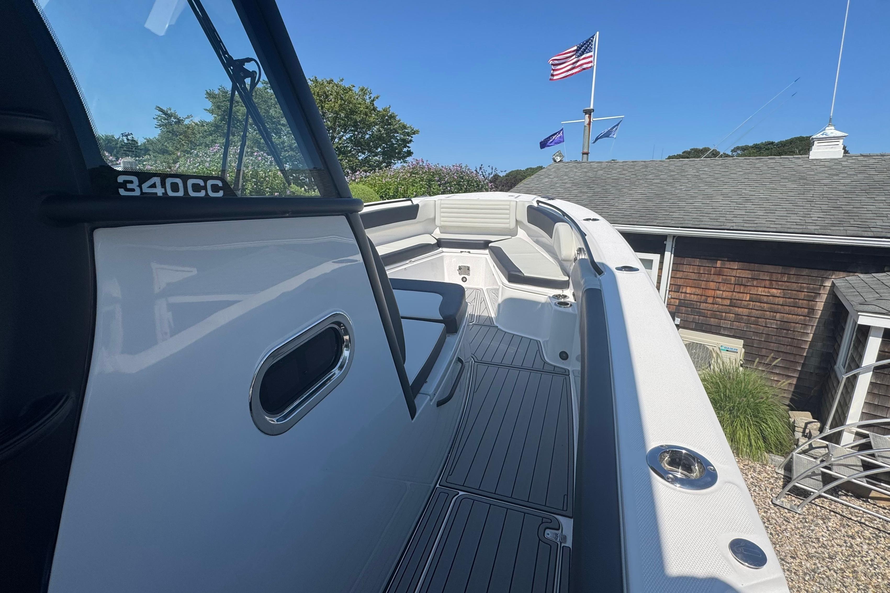 2025 Edgewater 340CC boat deck with seating, docked near a building, flags waving.
