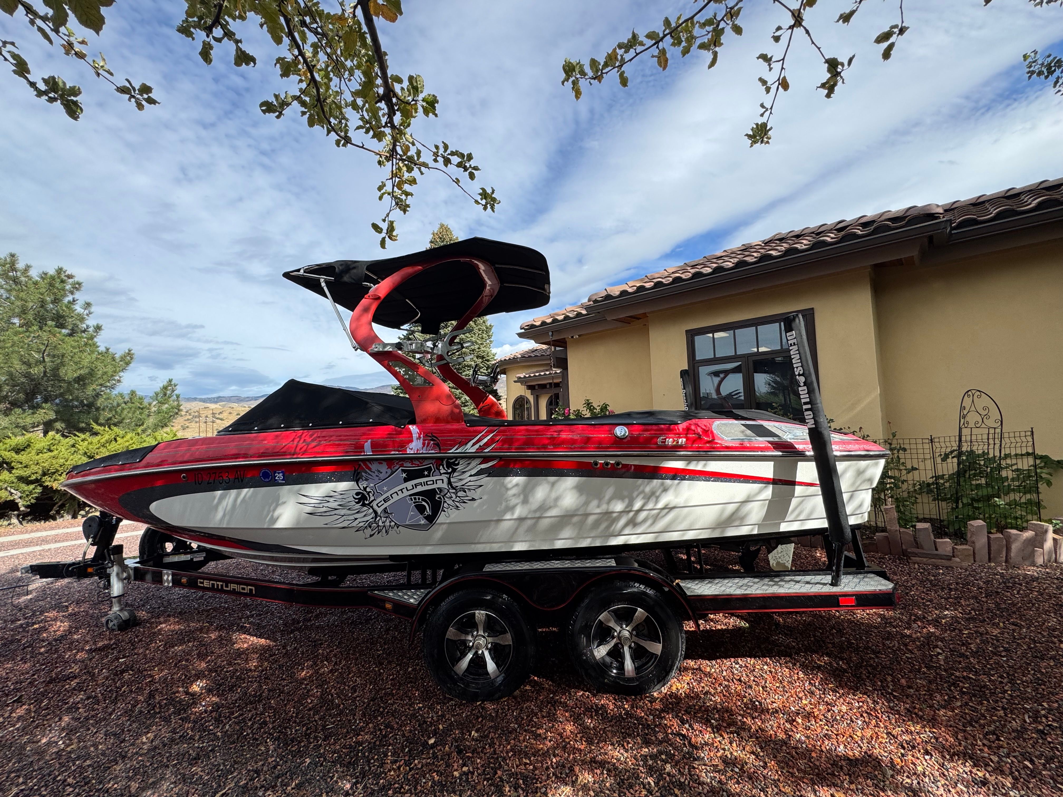 A red and white 2013 Centurion Enzo SV211 boat on a trailer in front of a house.