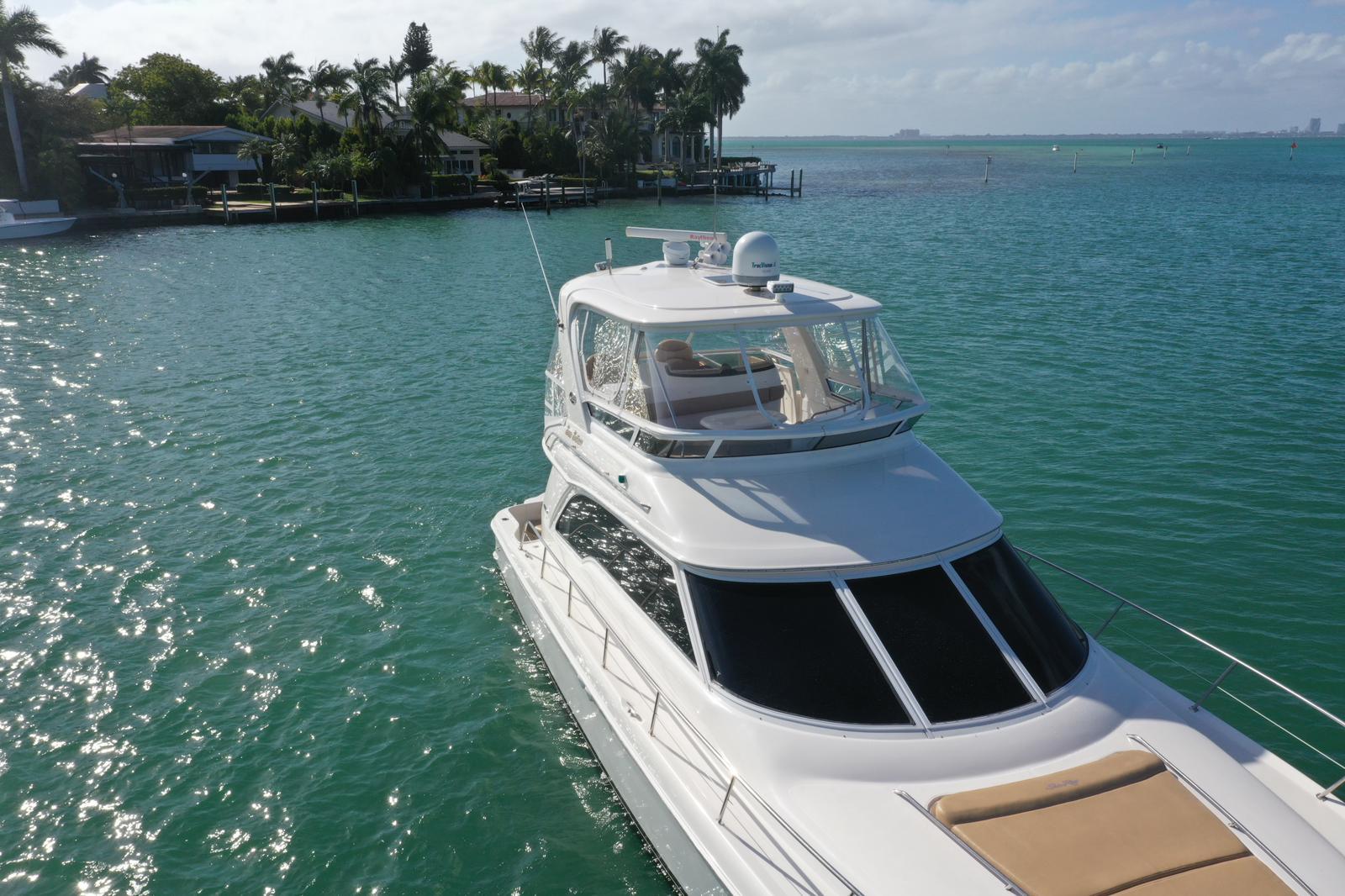 2001 Sea Ray 480 Sedan Bridge yacht cruising in turquoise waters near a tropical shoreline.