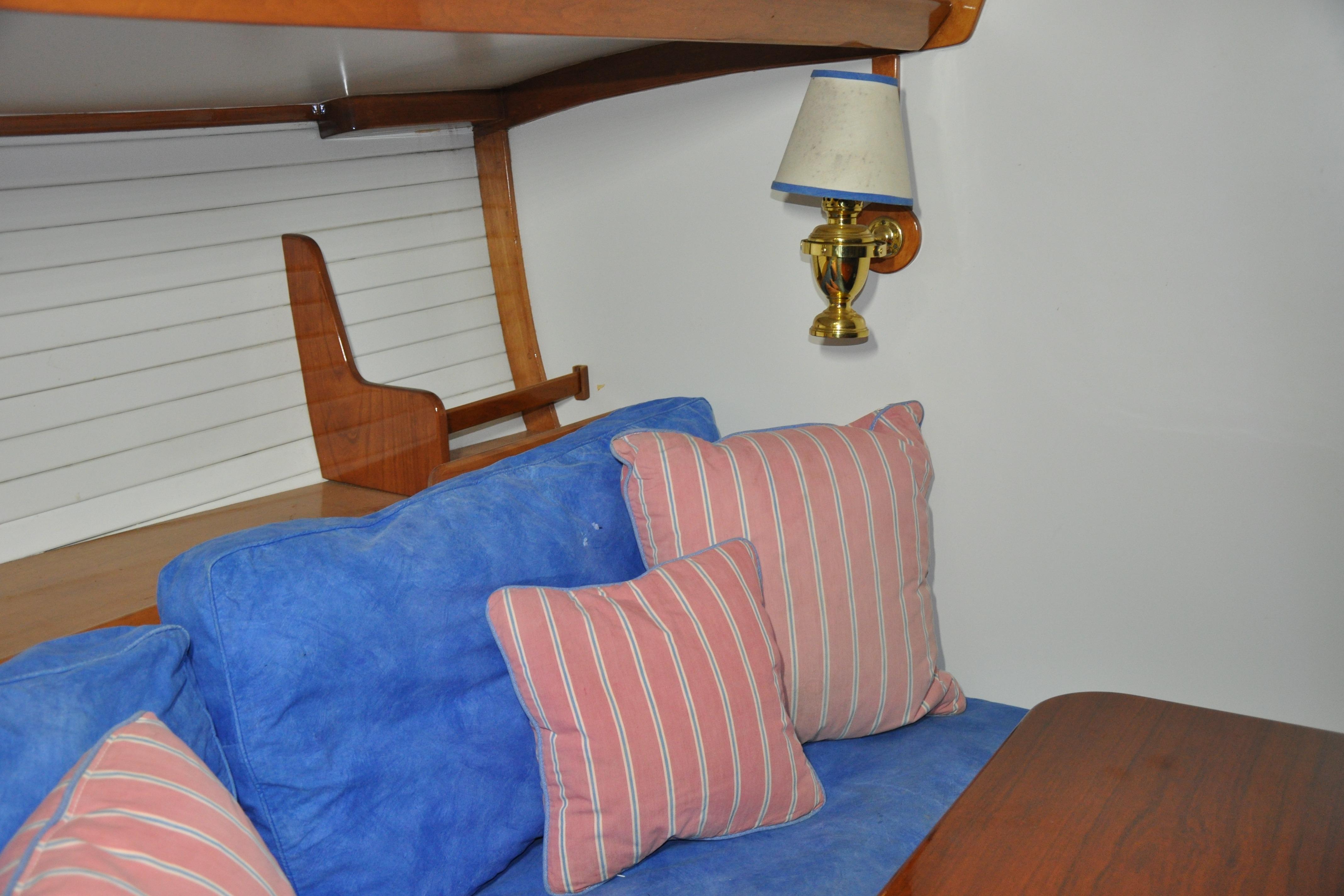 Interior of 1970 Hinckley Bermuda 40 with blue sofa, striped pillows, and brass wall lamp.