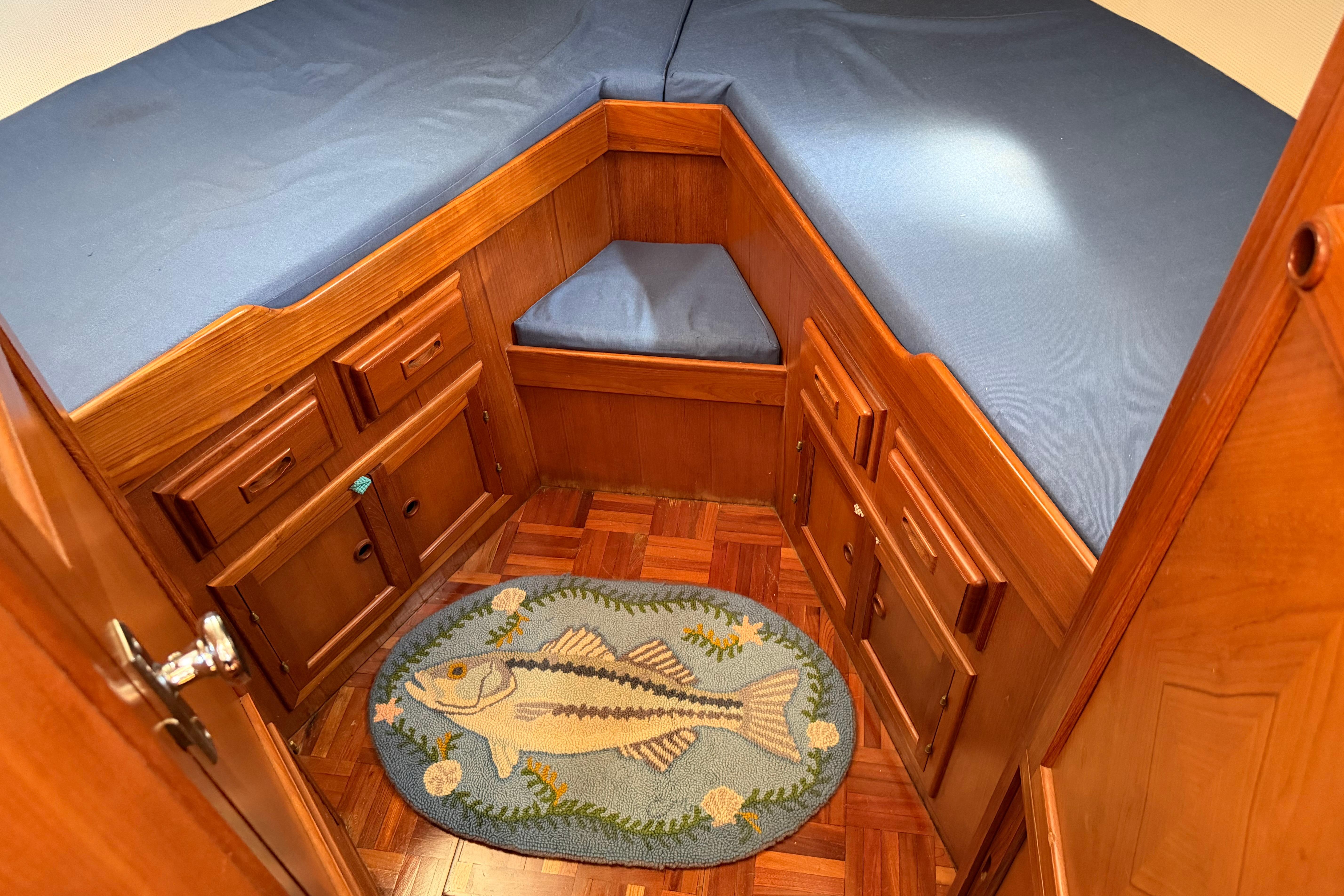 Cozy cabin interior of 1987 Marine Trader 36 with blue bedding and fish-themed rug.