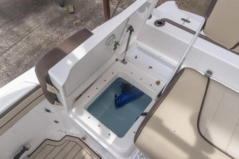 2023 Yamaha Boats 195 FSH Sport storage compartment with blue hose and seating area.