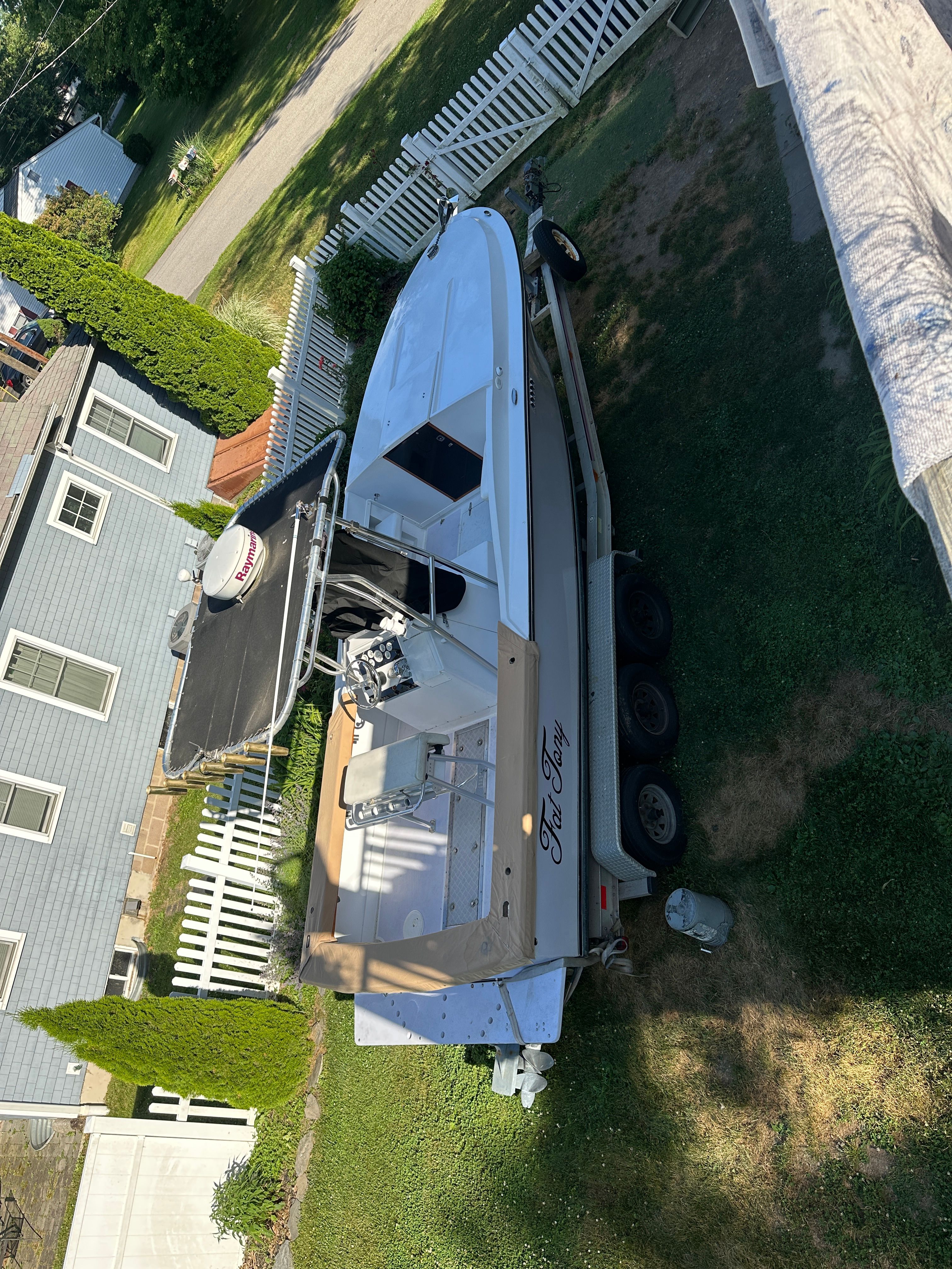 A white boat is on a trailer in a yard next to a house.