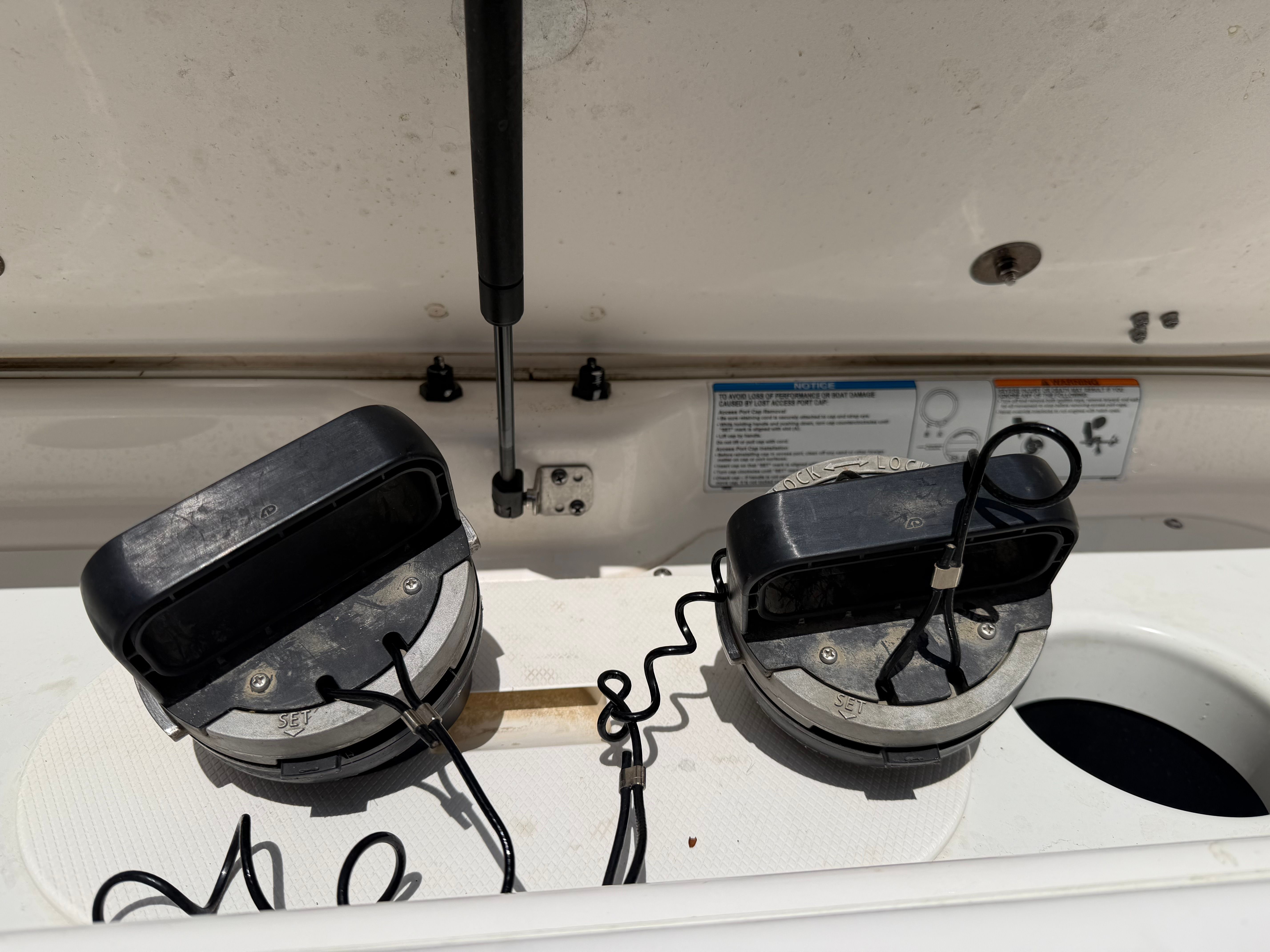 Two black boat speakers are mounted on a white surface, surrounded by cables and a hydraulic arm.