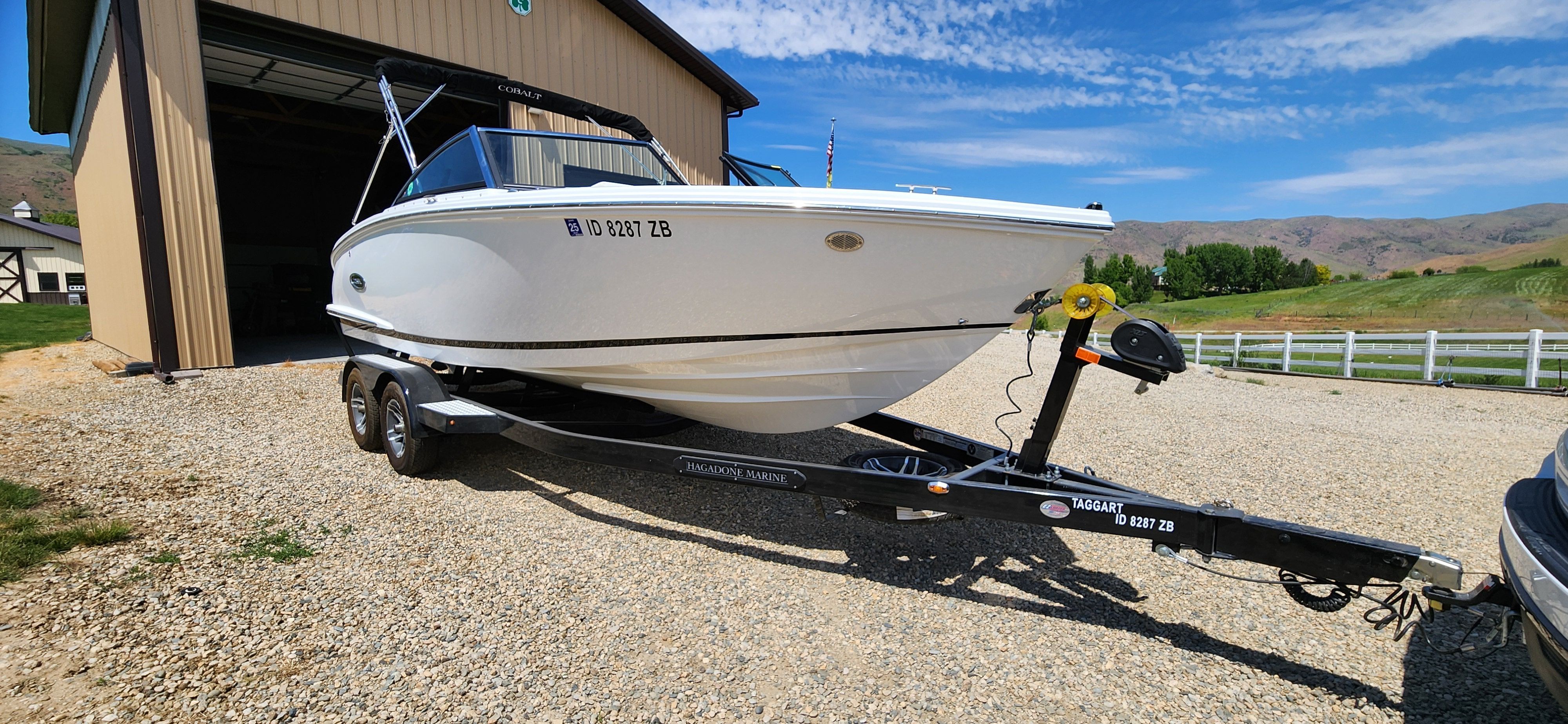 A white Cobalt CS22 boat on a trailer in front of a barn.