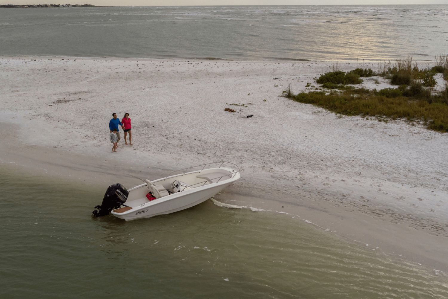 A Boston Whaler 160 Super Sport is beached on the shore. Two people walk along the water's edge.