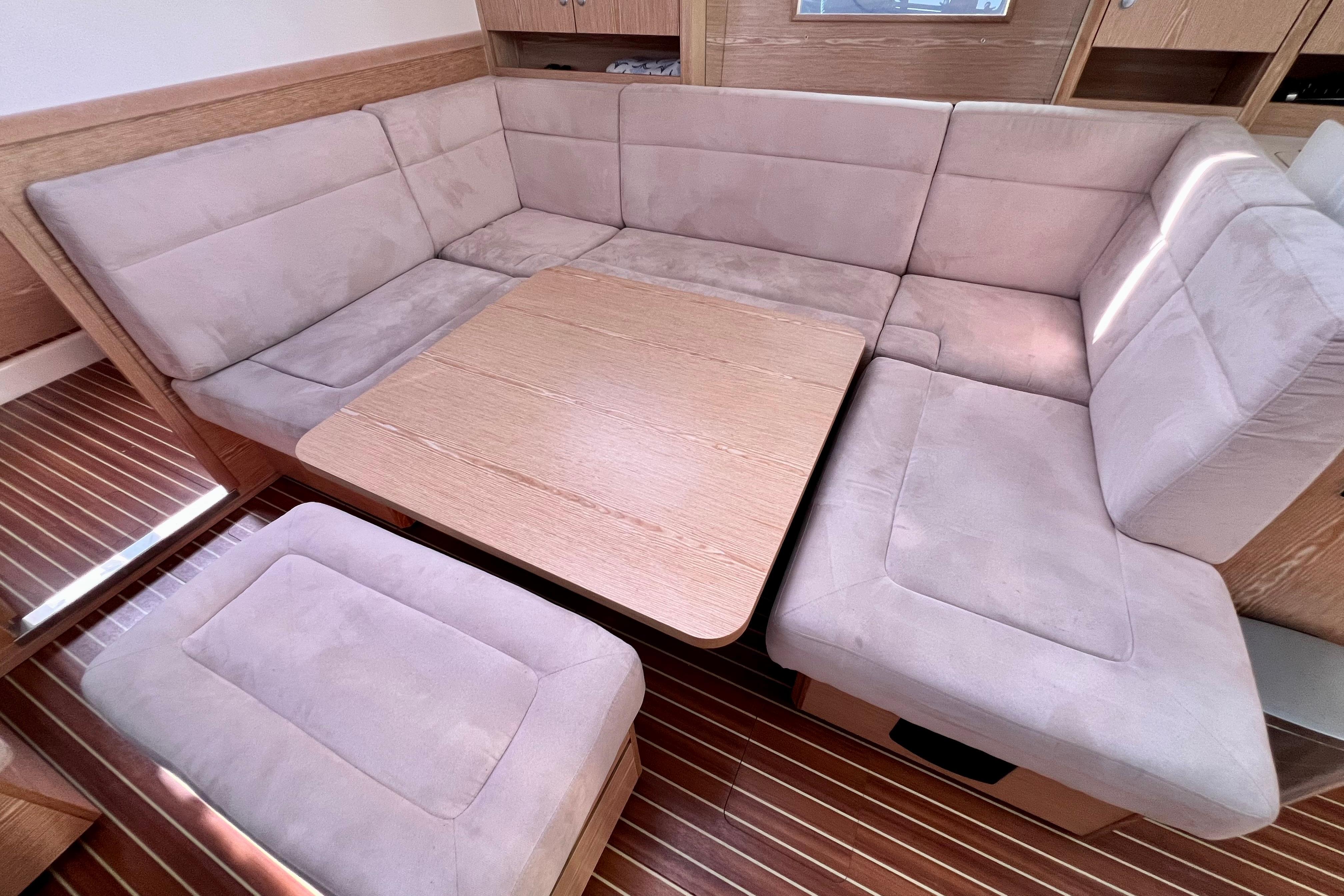 Interior of 2016 Hanse 455 yacht with beige cushioned seating and wooden table.