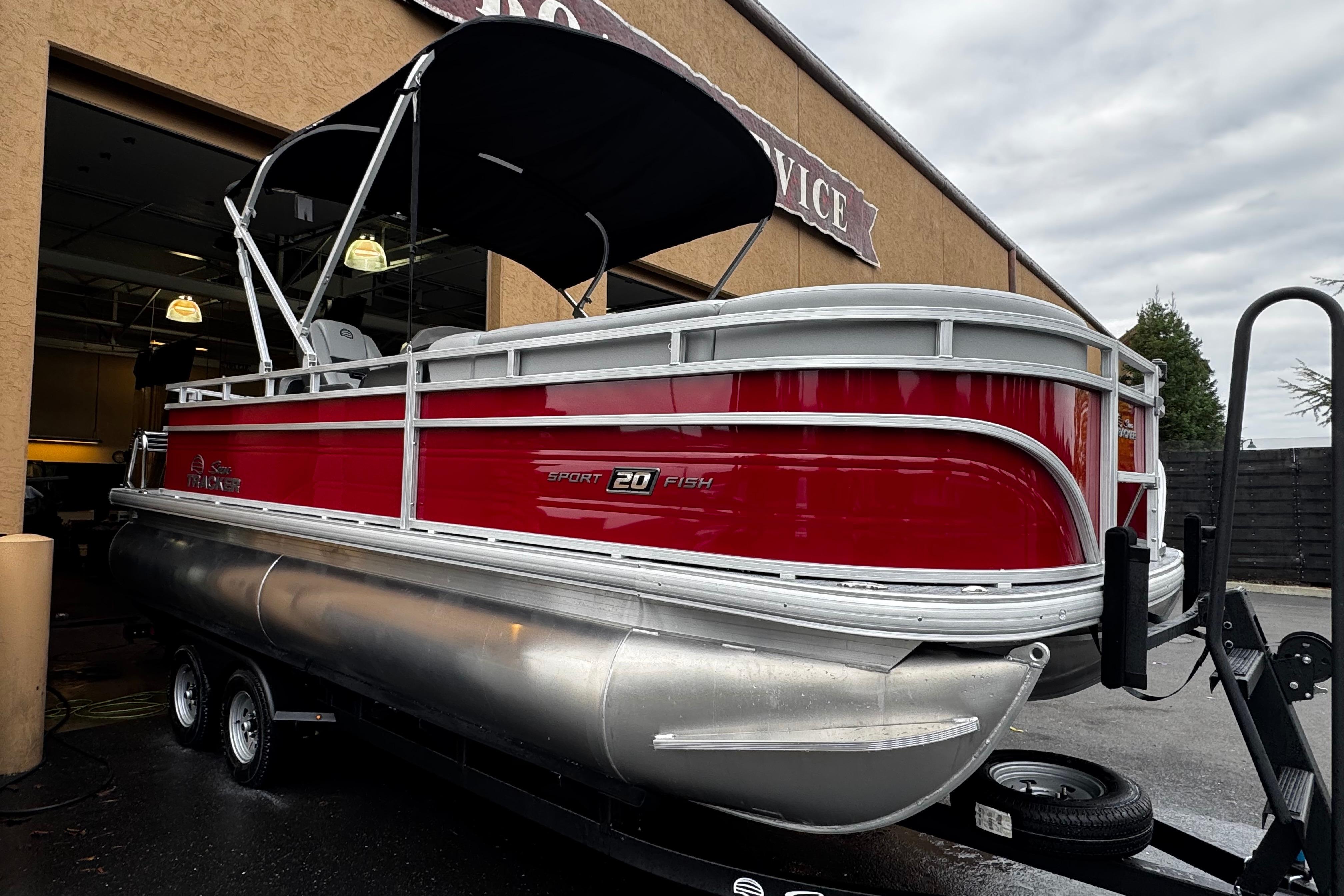 2026 Sun Tracker SportFish 20 DLX pontoon boat with red exterior, parked outside a service building.