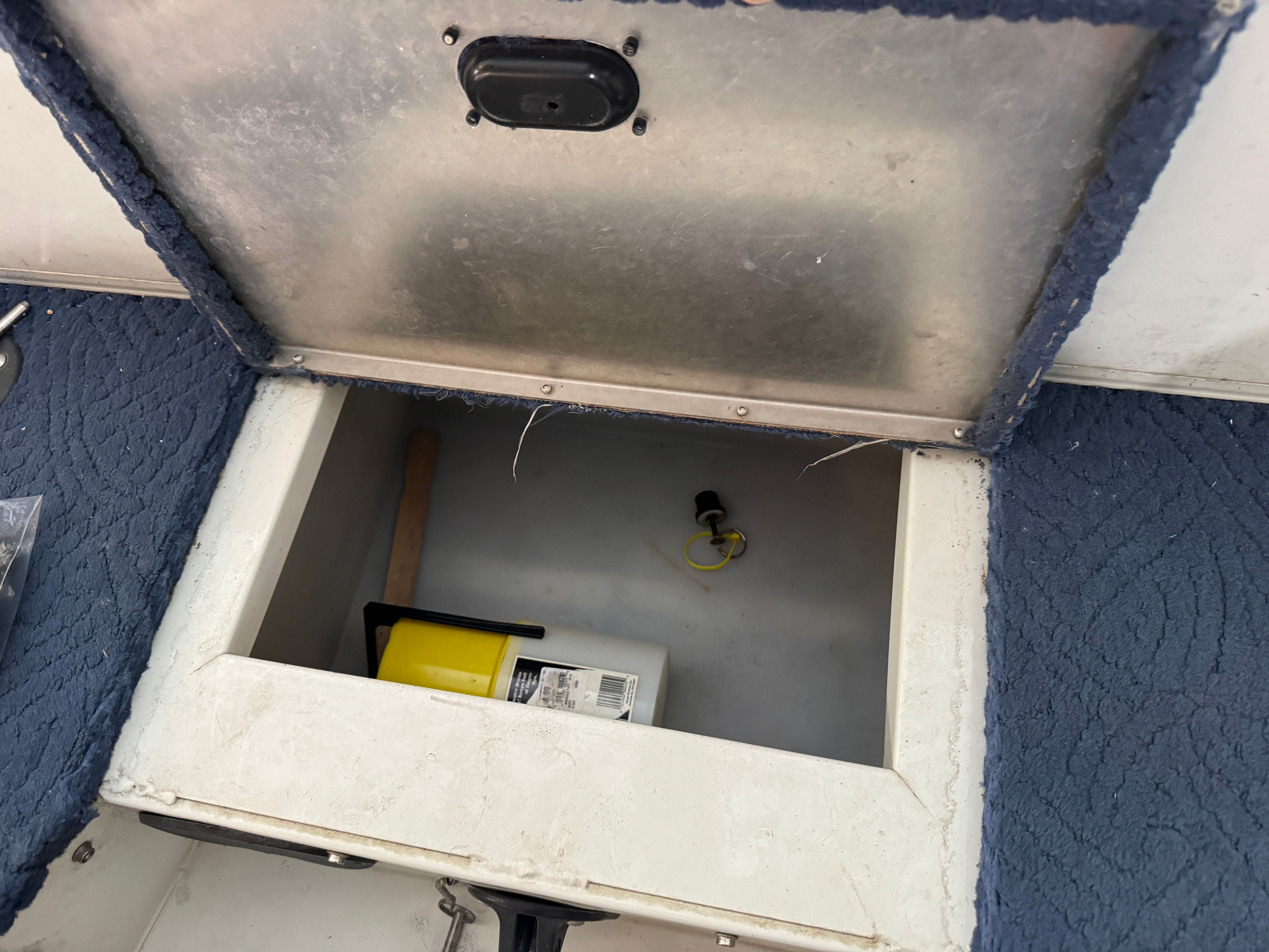 An open storage compartment on a boat with a yellow container and a small item.