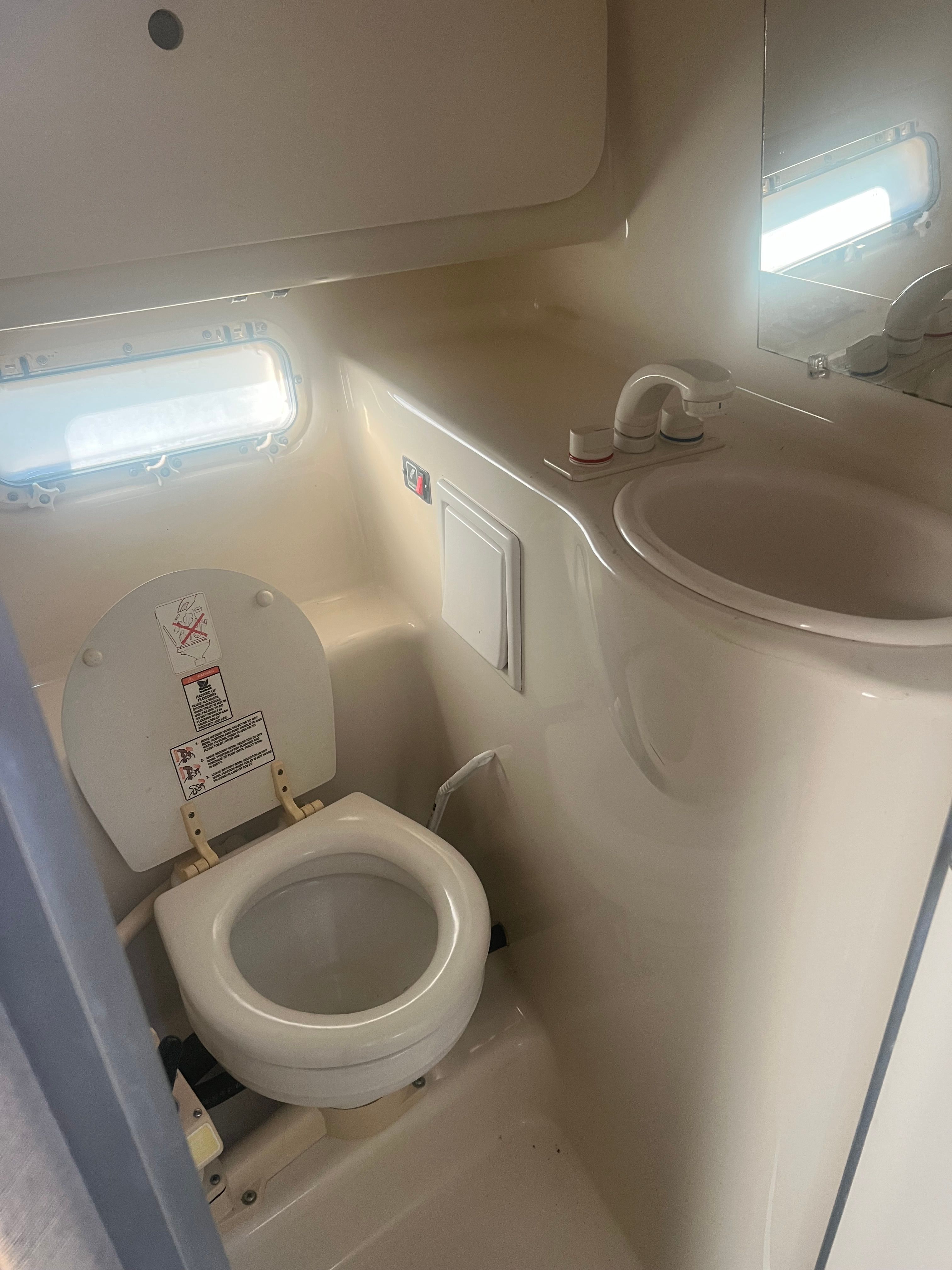 The image shows a compact boat toilet with a sink and small window.