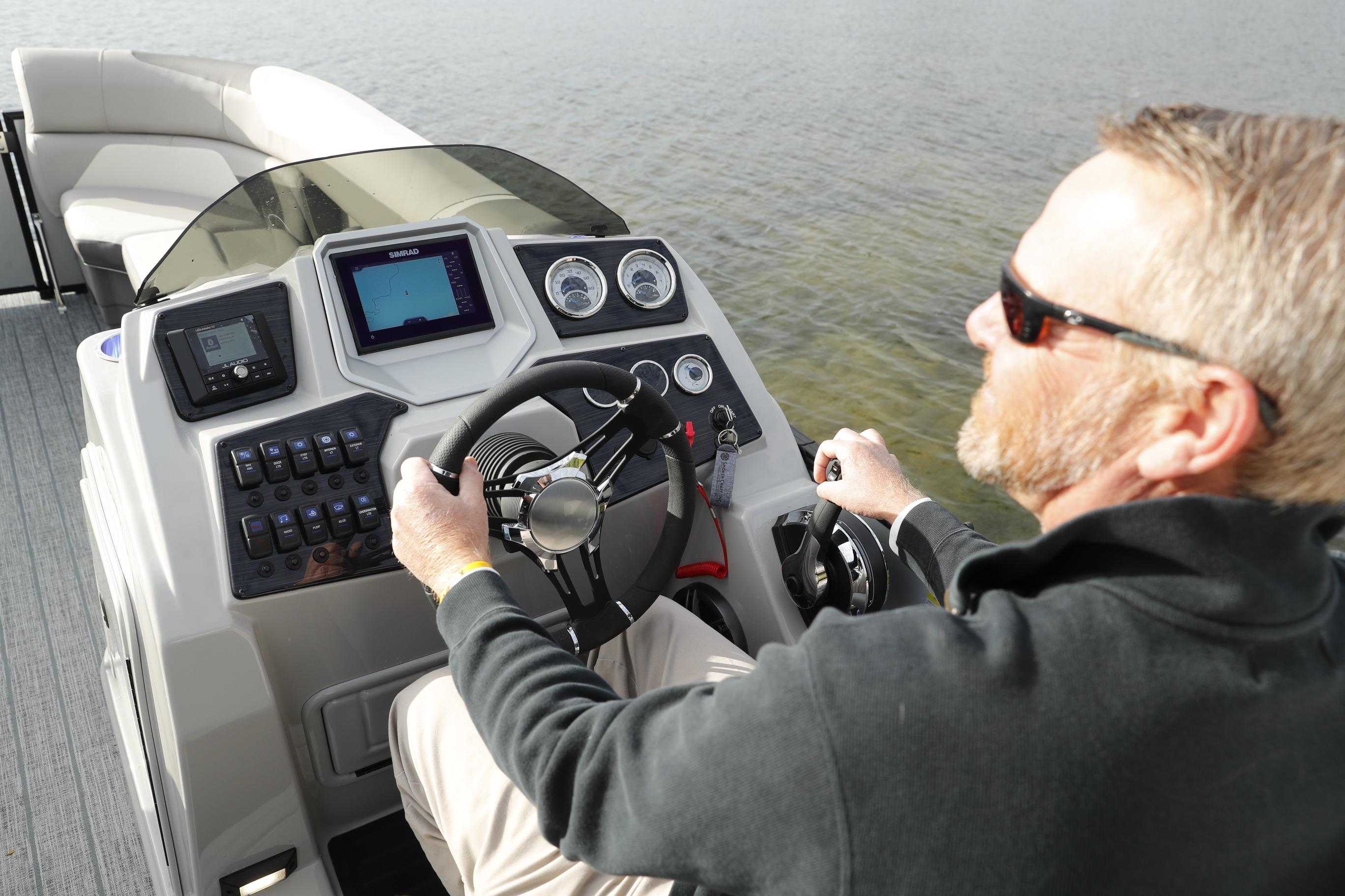 Man steering 2026 SunChaser Eclipse 25 LR DH pontoon boat on water.
