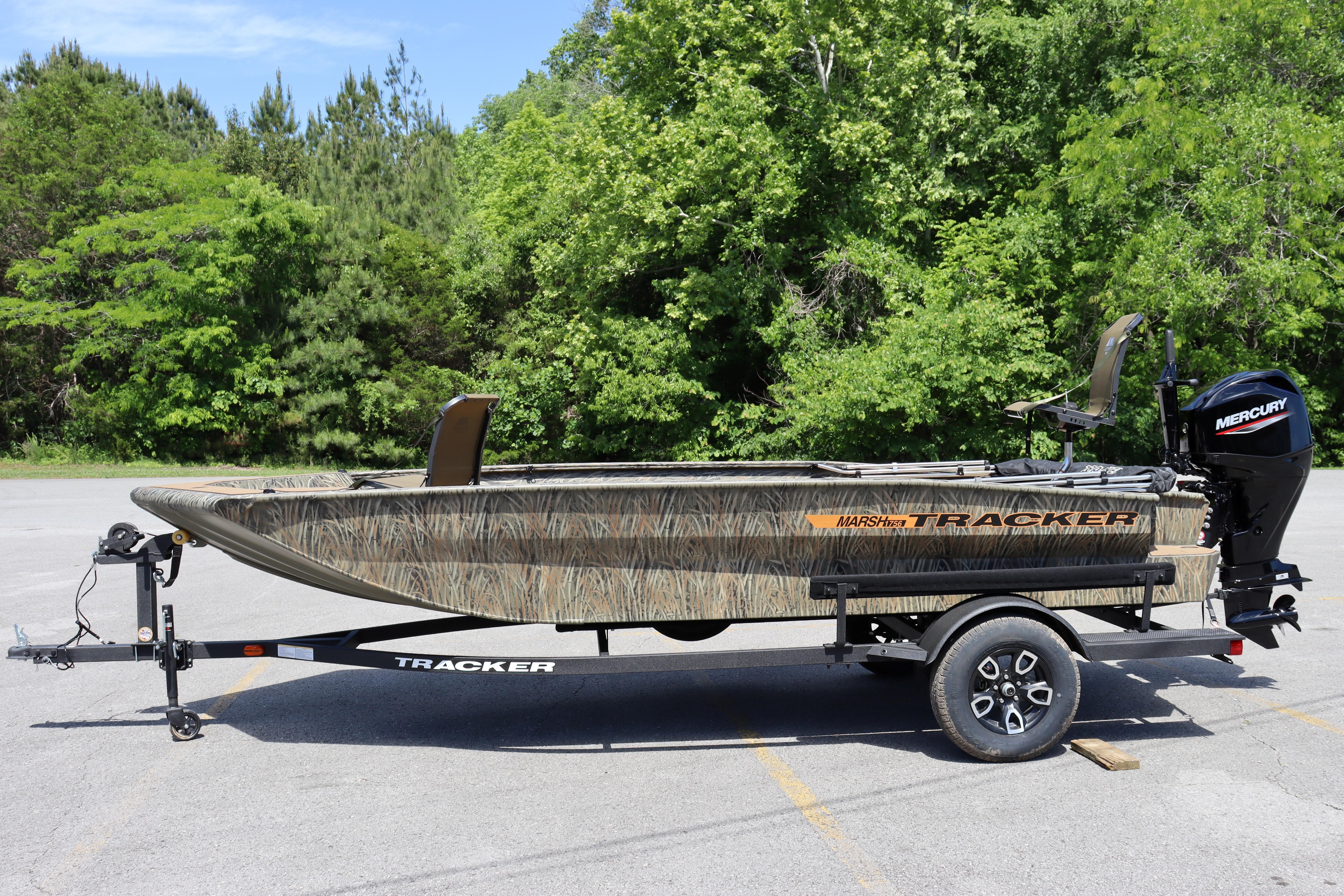 2026 Tracker Grizzly 1756 T Marsh boat on trailer, parked outdoors with green trees in background.