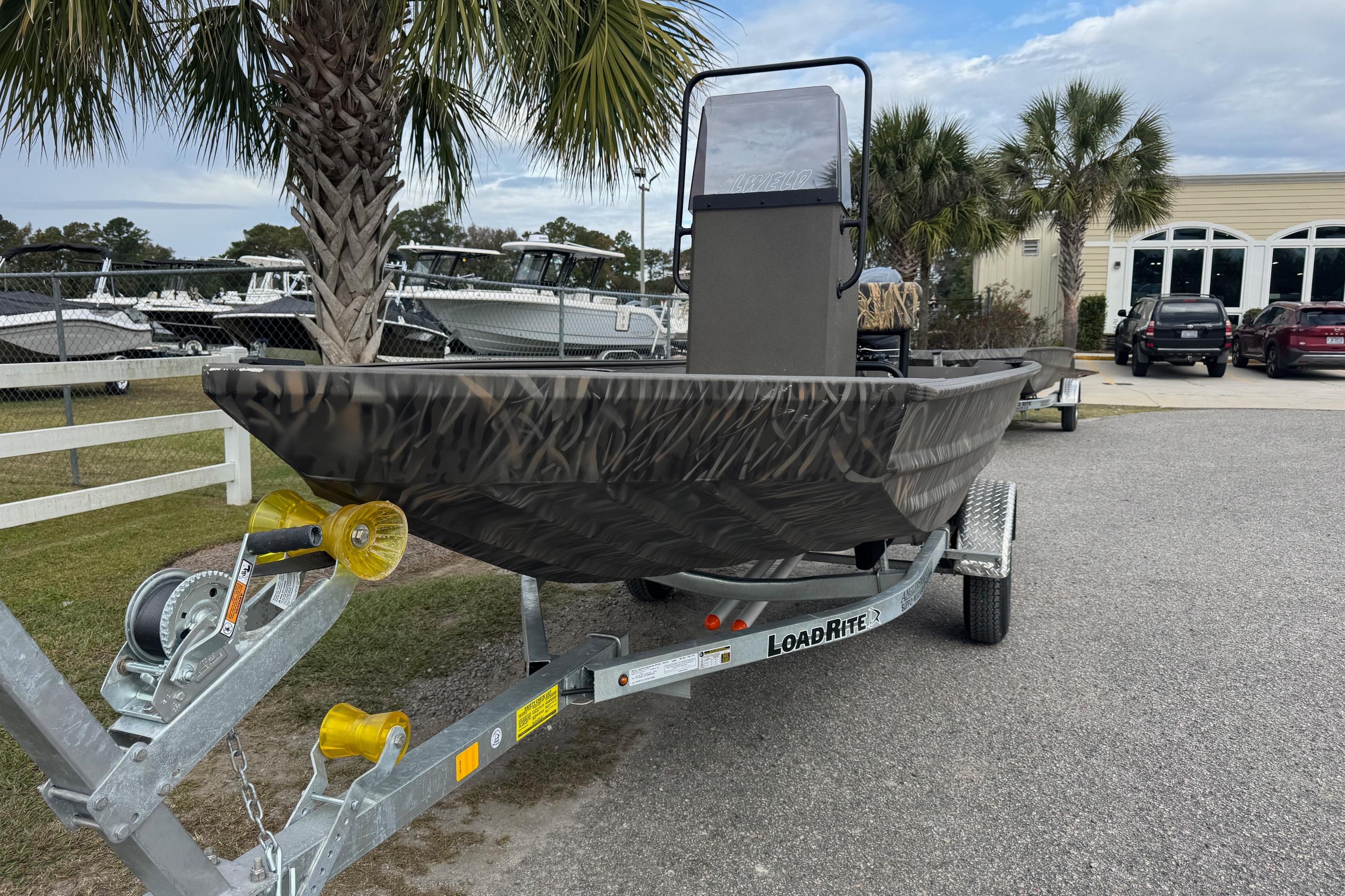 2026 Alweld 1656VV Marsh Console CC boat on Load Rite trailer, parked near palm trees.
