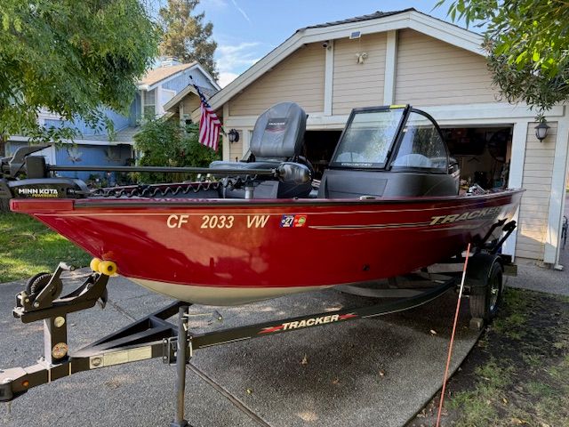 A red Tracker boat is on a trailer in front of a house.