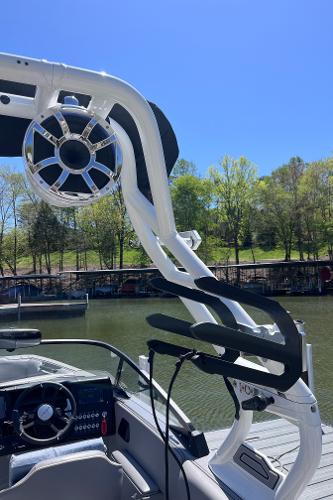 2024 Moomba Max boat with wakeboard tower and speaker, docked by a scenic lake.