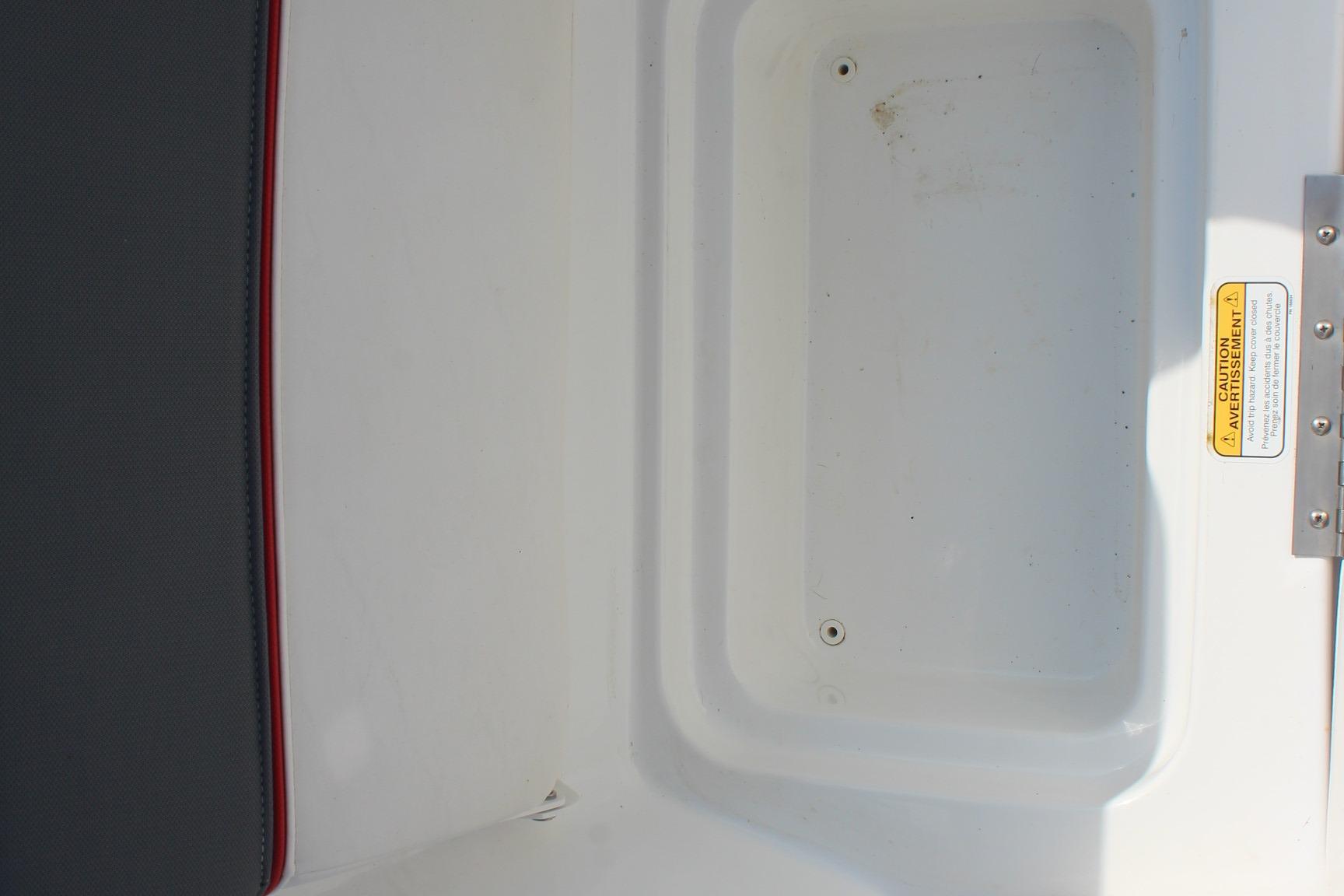 2023 Tahoe T16 boat storage compartment with caution label and black-red seat edge.