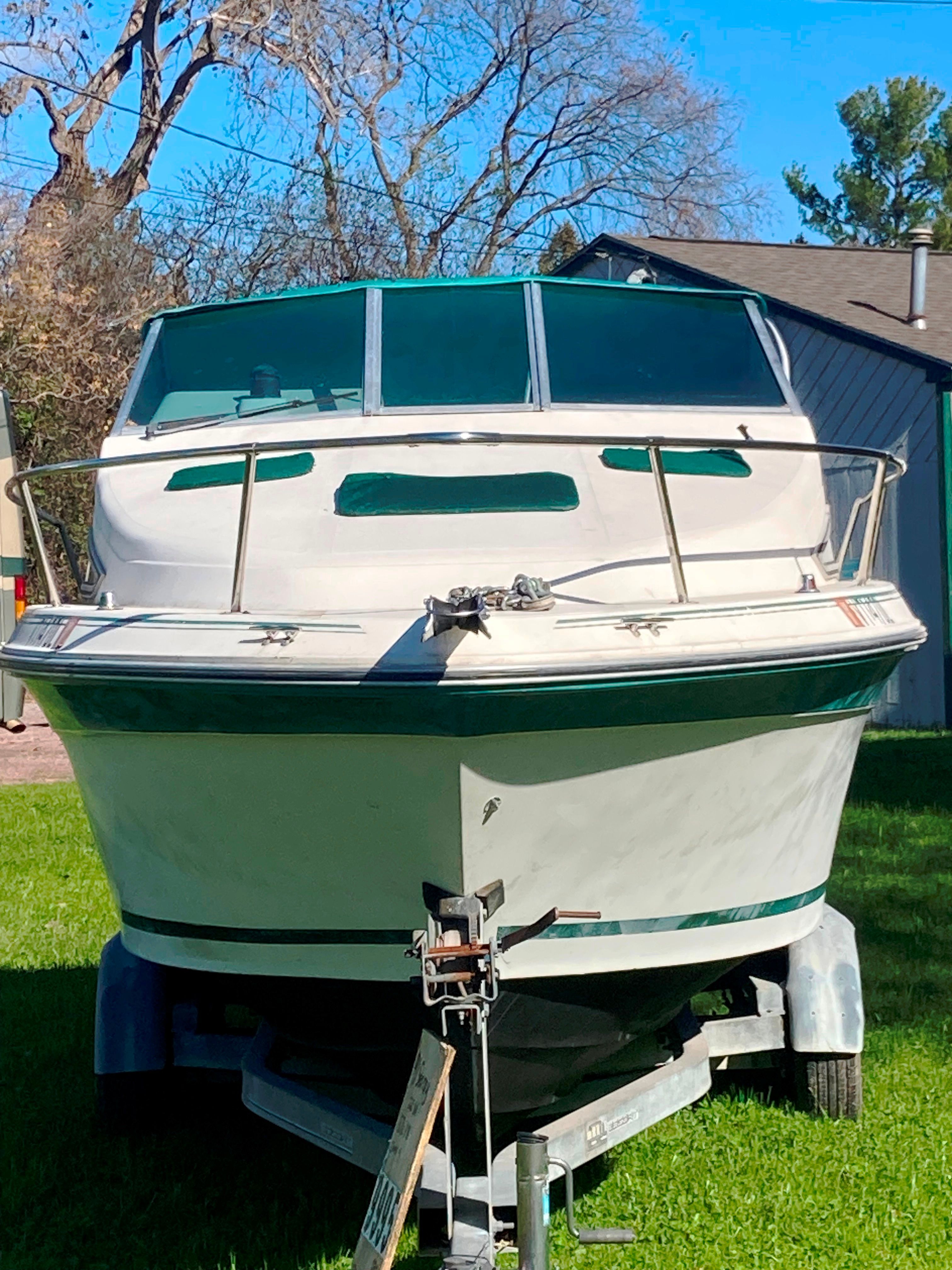 A 1991 Sea Ray 220 Sundancer on a trailer outdoors, surrounded by trees.