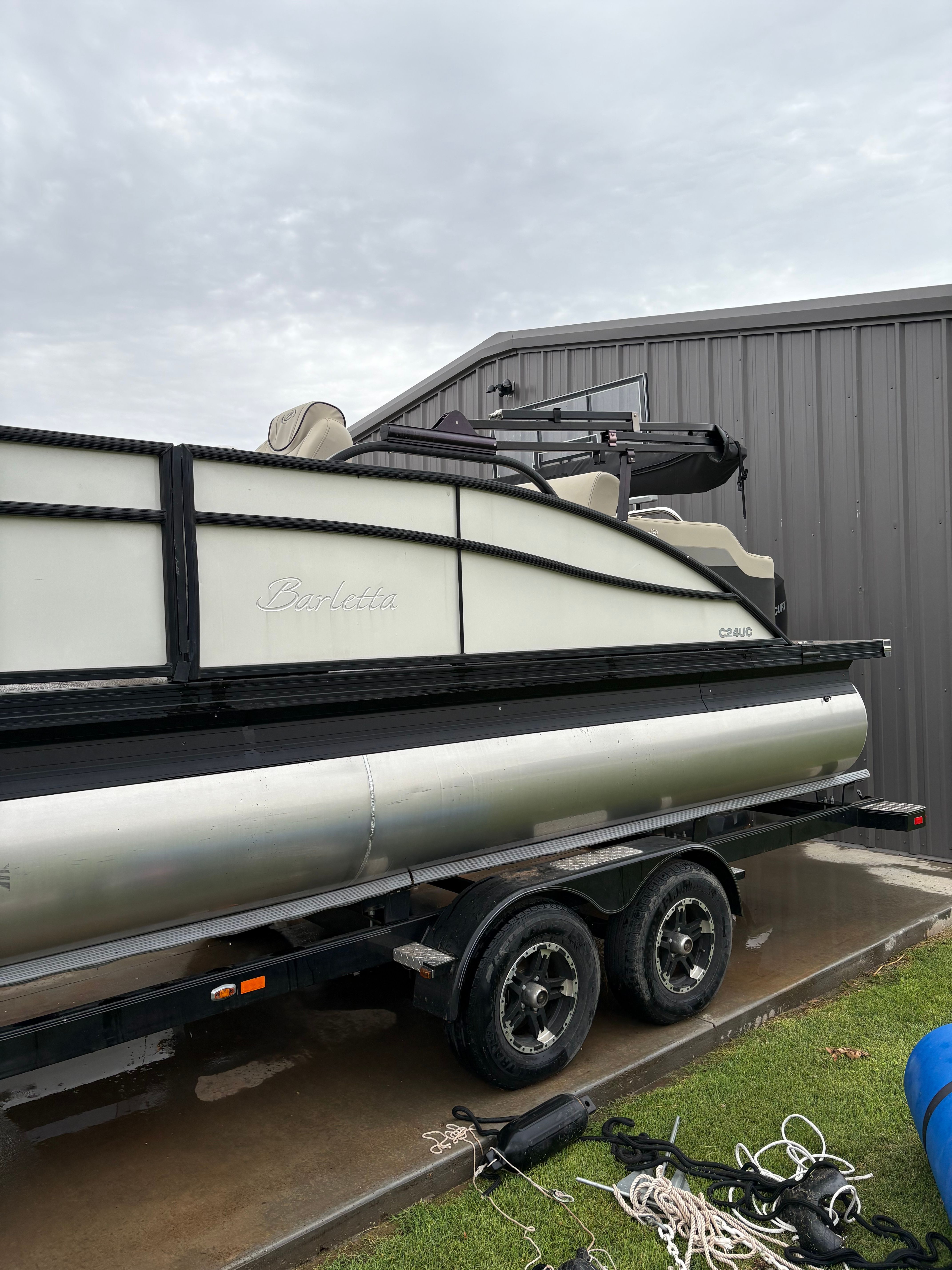 A Barletta pontoon boat on a trailer, parked beside a building.
