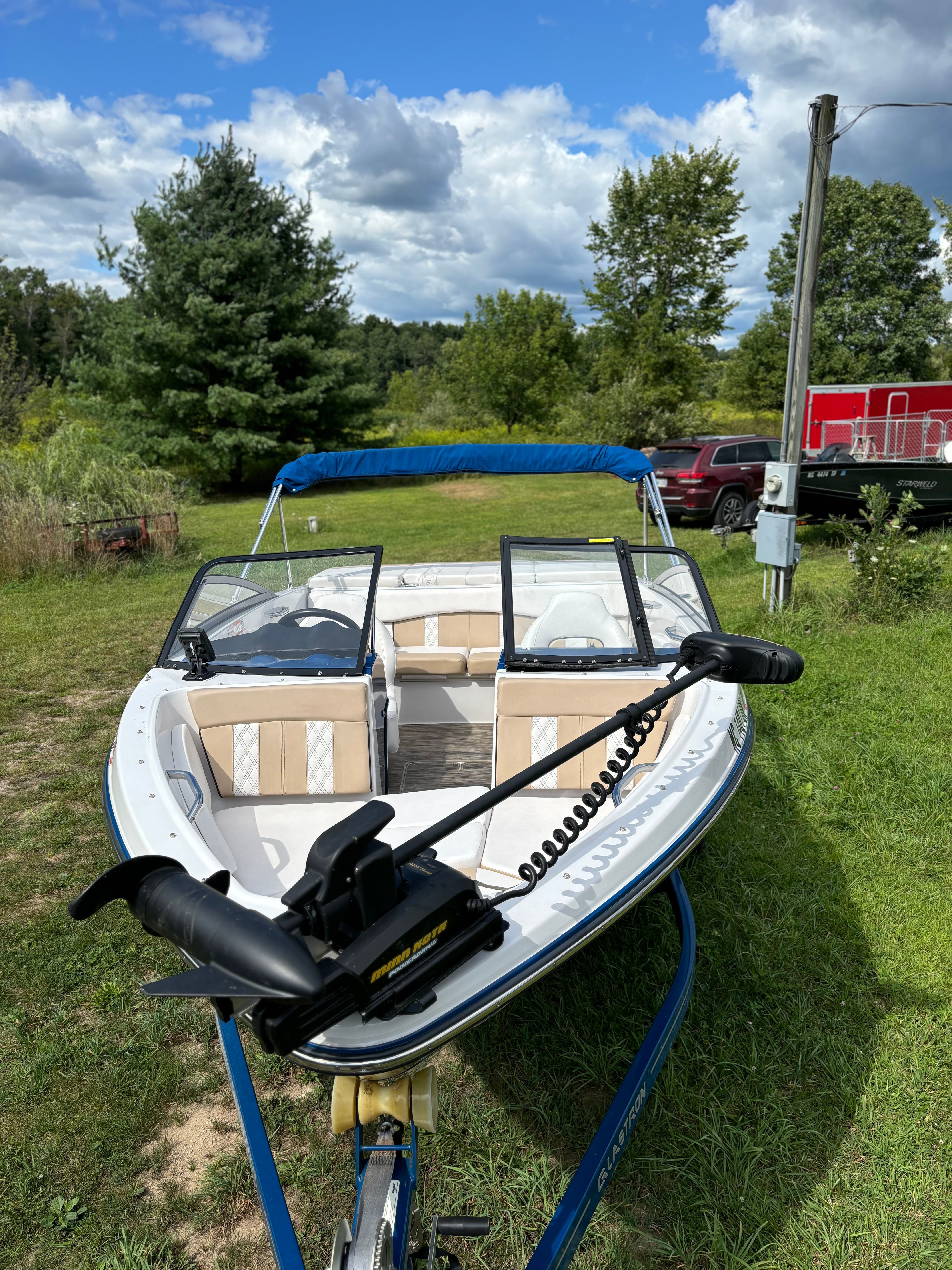 A Glastron GTSF 185 boat is on a trailer on a grassy area.