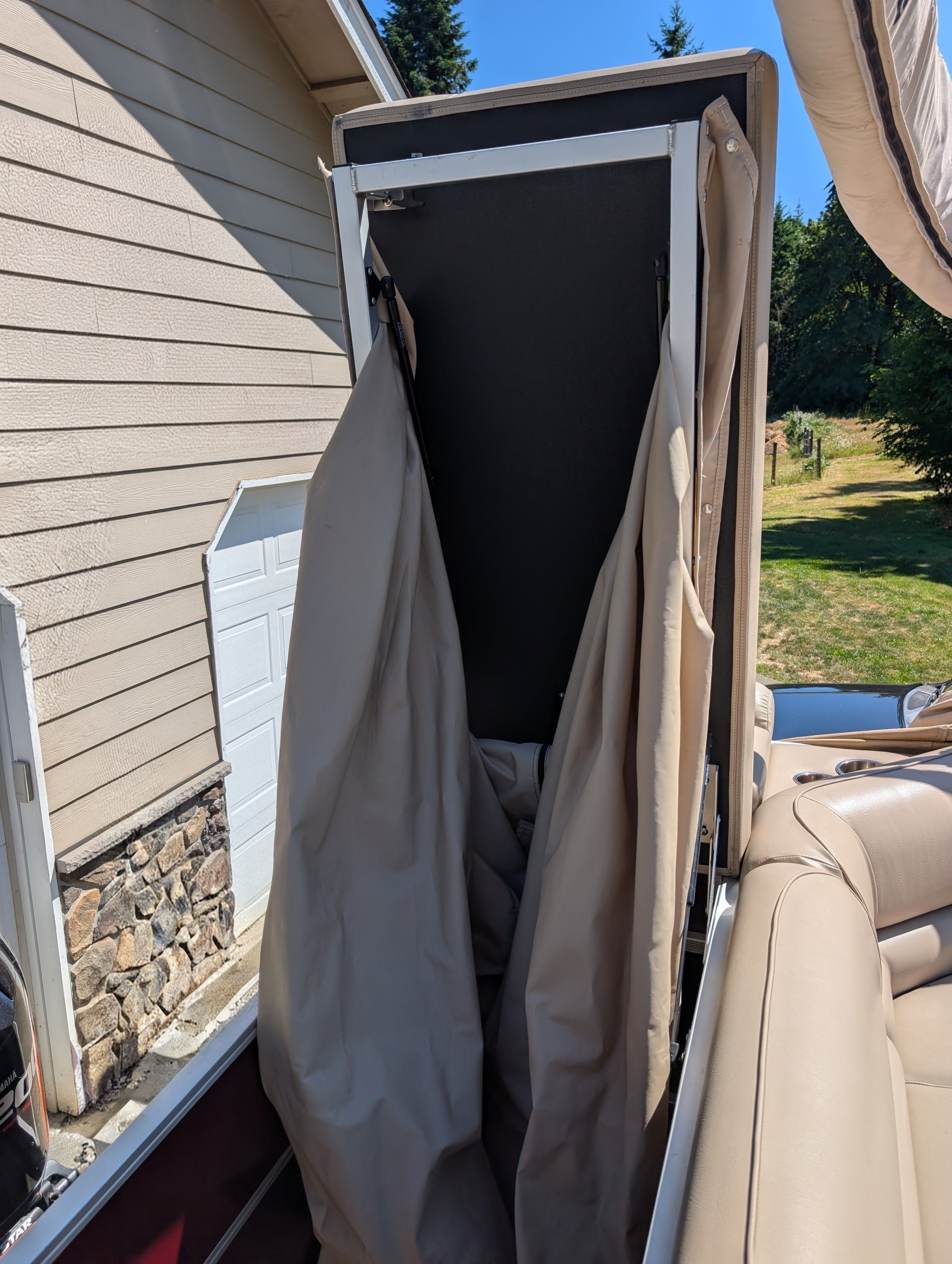 A collapsible changing area on a boat with beige curtains and cushioned seating.