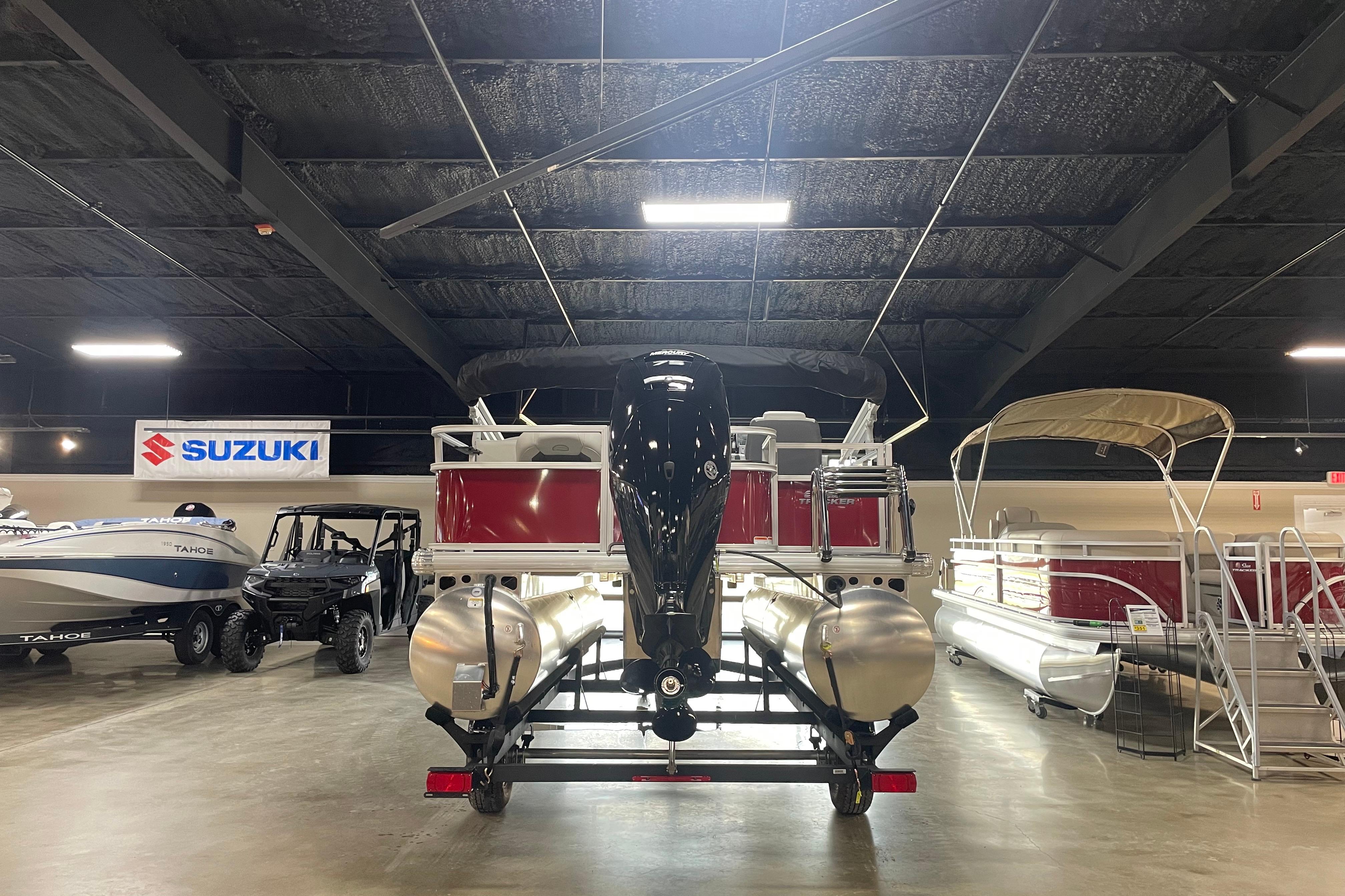 2026 Sun Tracker Bass Buggy 18 DLX pontoon boat in showroom with Suzuki sign.