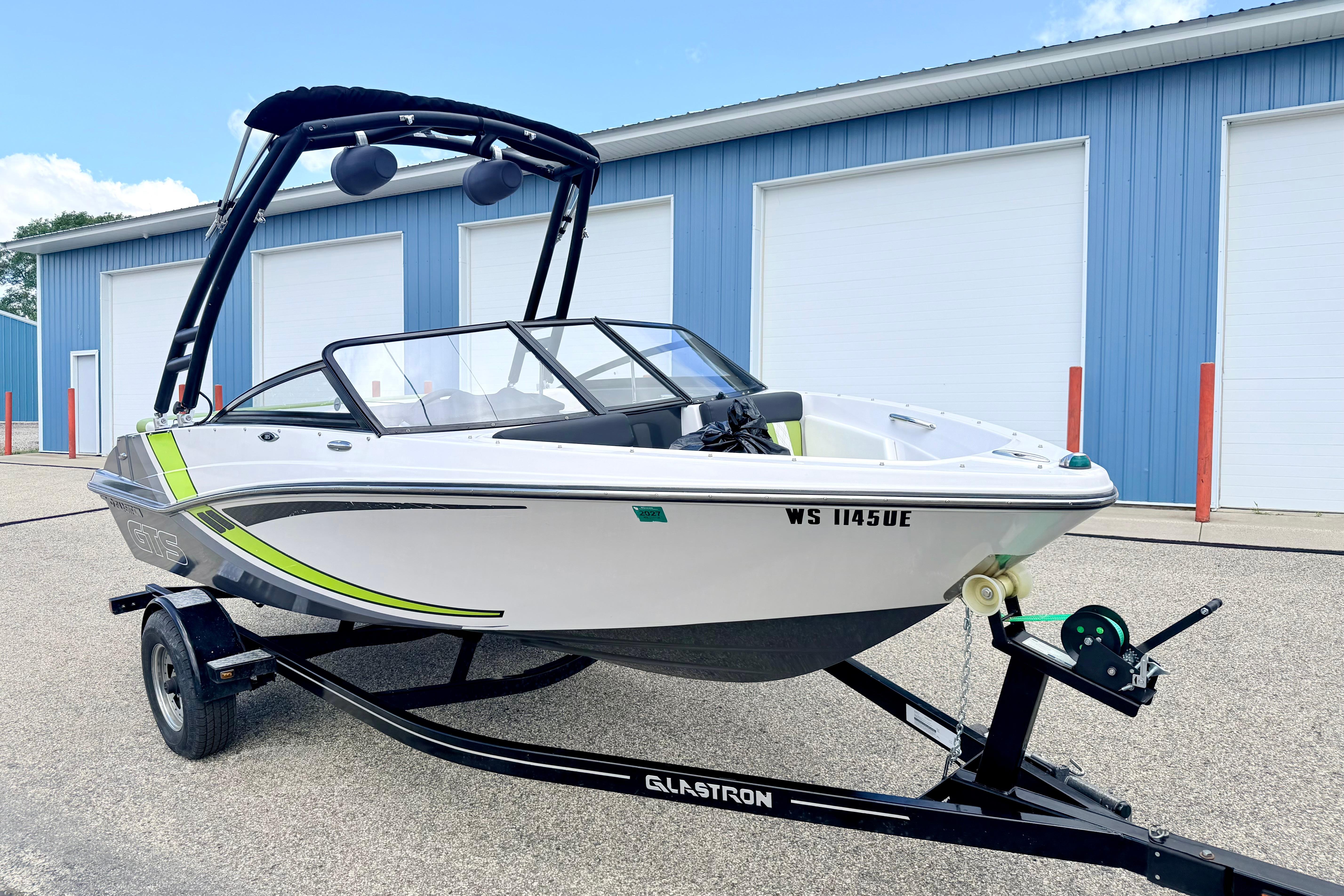 2018 Glastron GT 185 boat on trailer, parked outside blue warehouse.