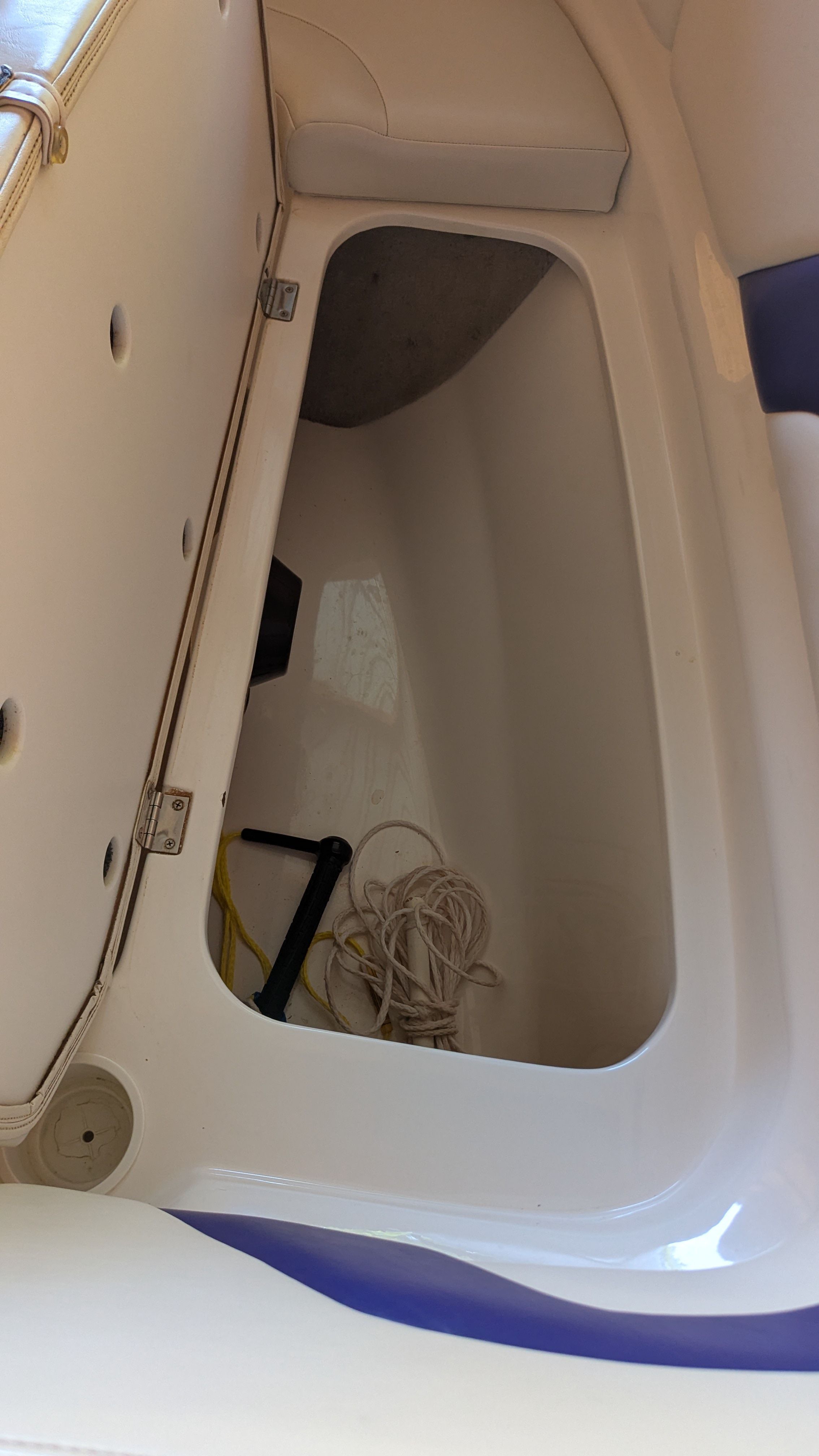 An open storage compartment inside a boat with ropes and a black object.