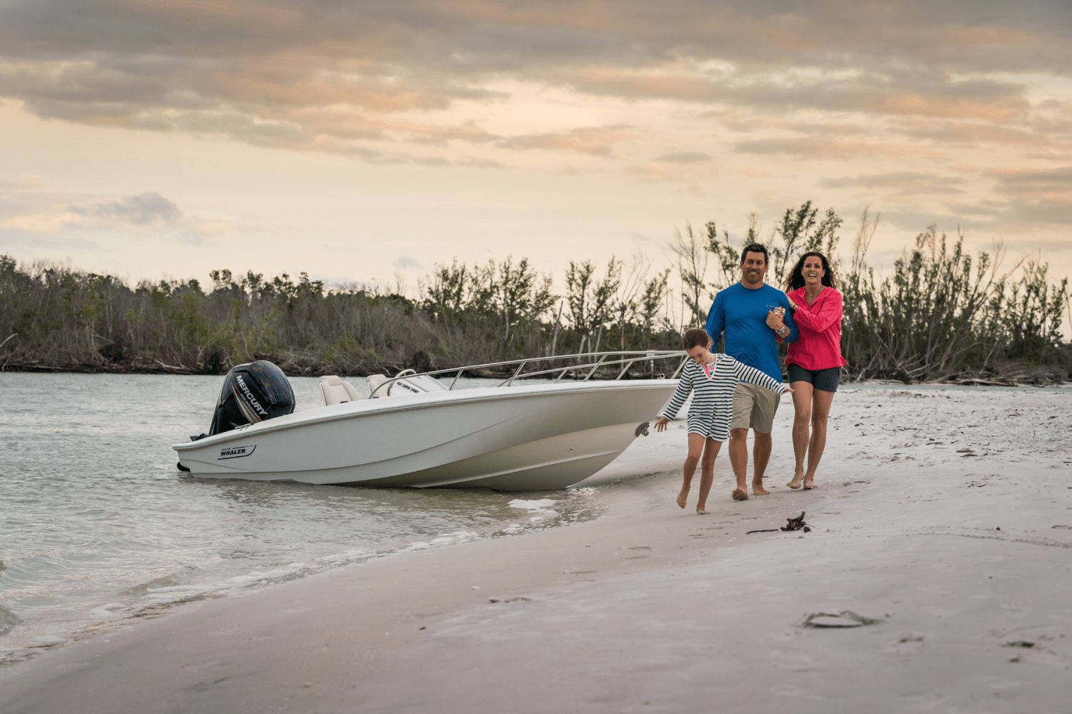 A family walks on the beach beside a Boston Whaler 160 Super Sport boat.
