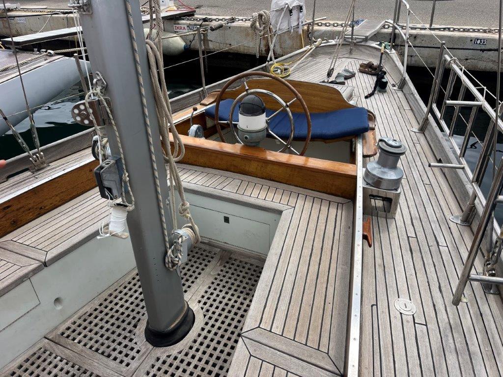 1958 Costantini ketch sailboat with wooden deck and steering wheel in marina.