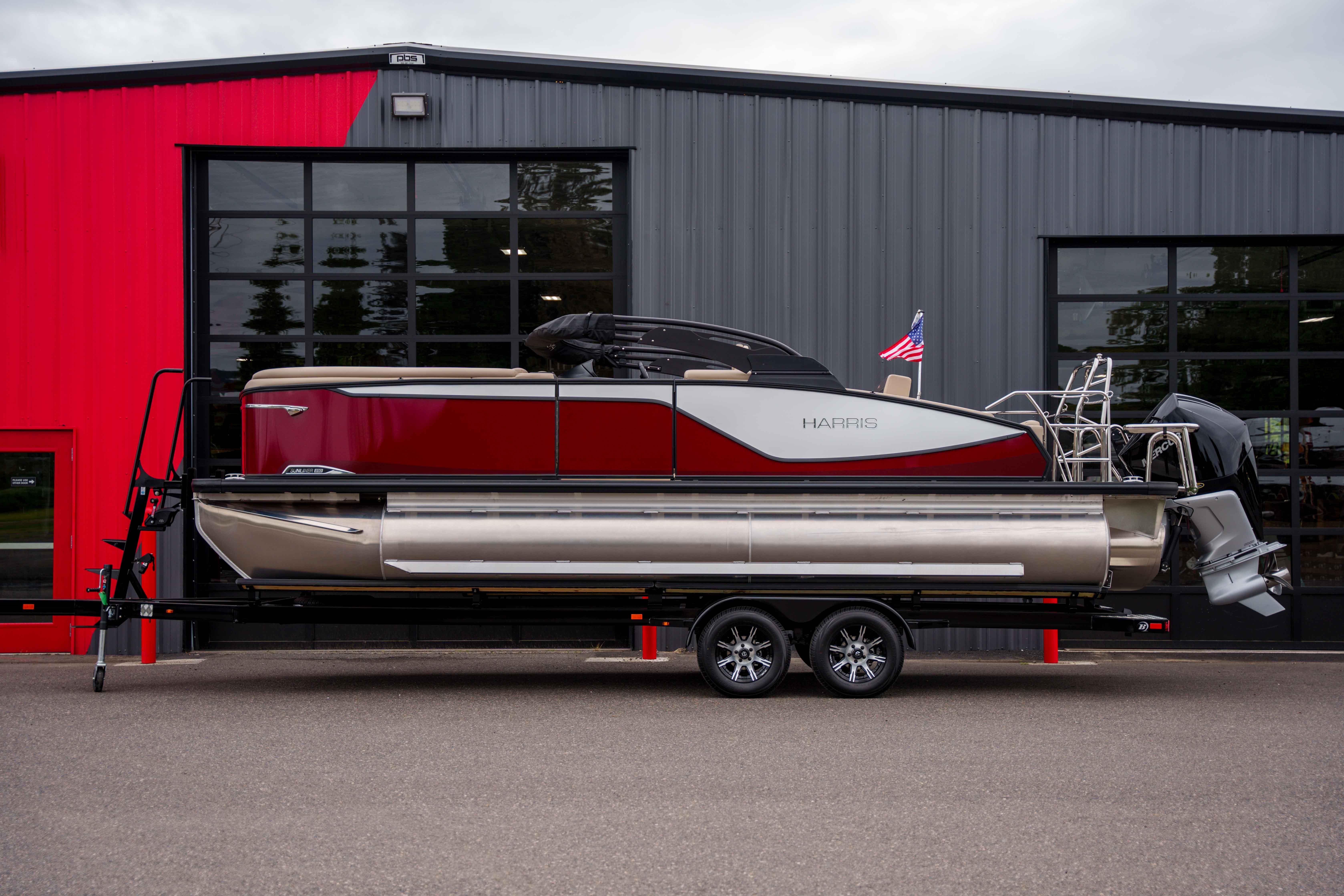 2026 Harris Sunliner 230 pontoon boat on trailer, parked outside a modern building.