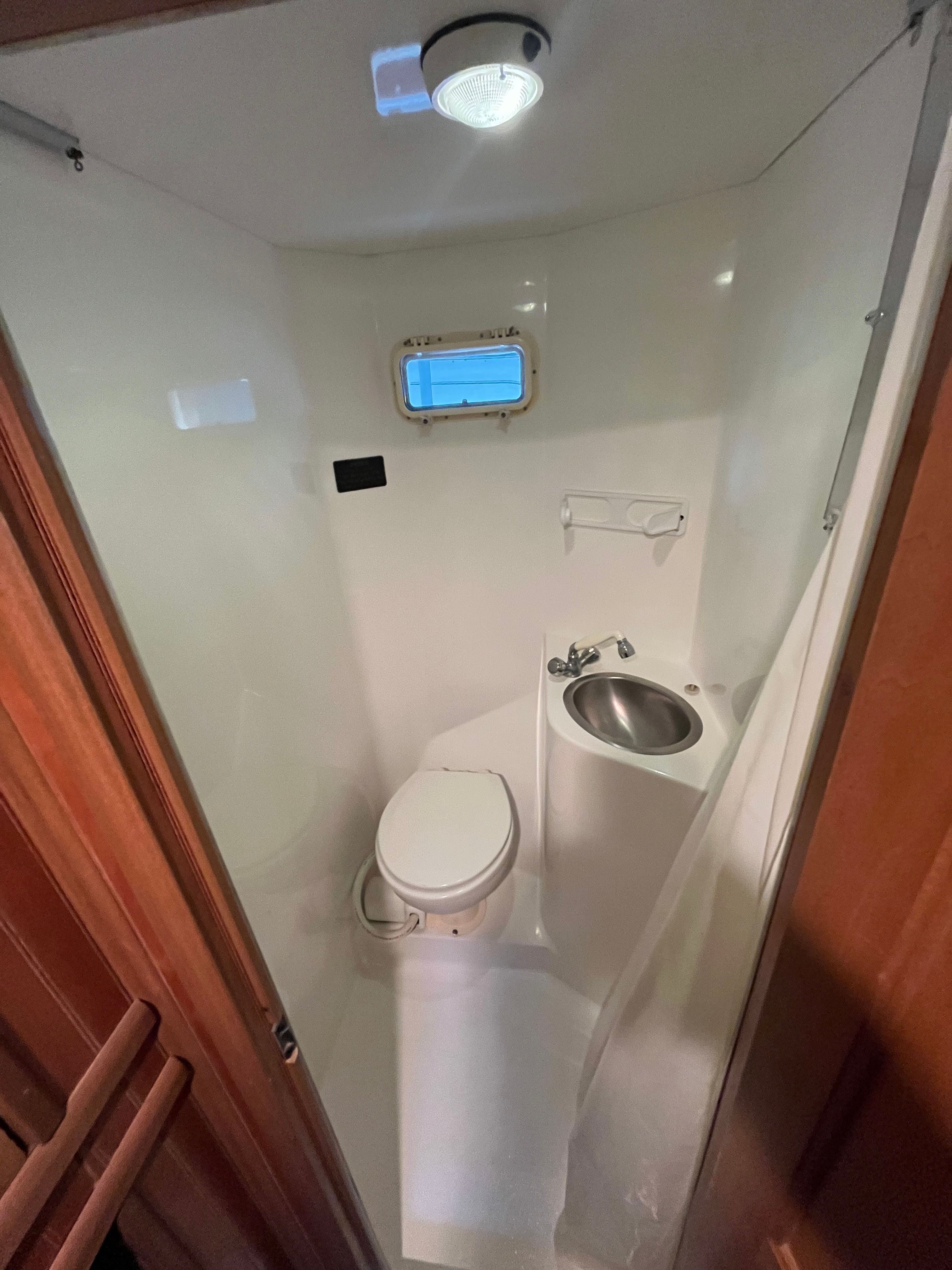 Compact bathroom with toilet, sink, and small window on a boat.