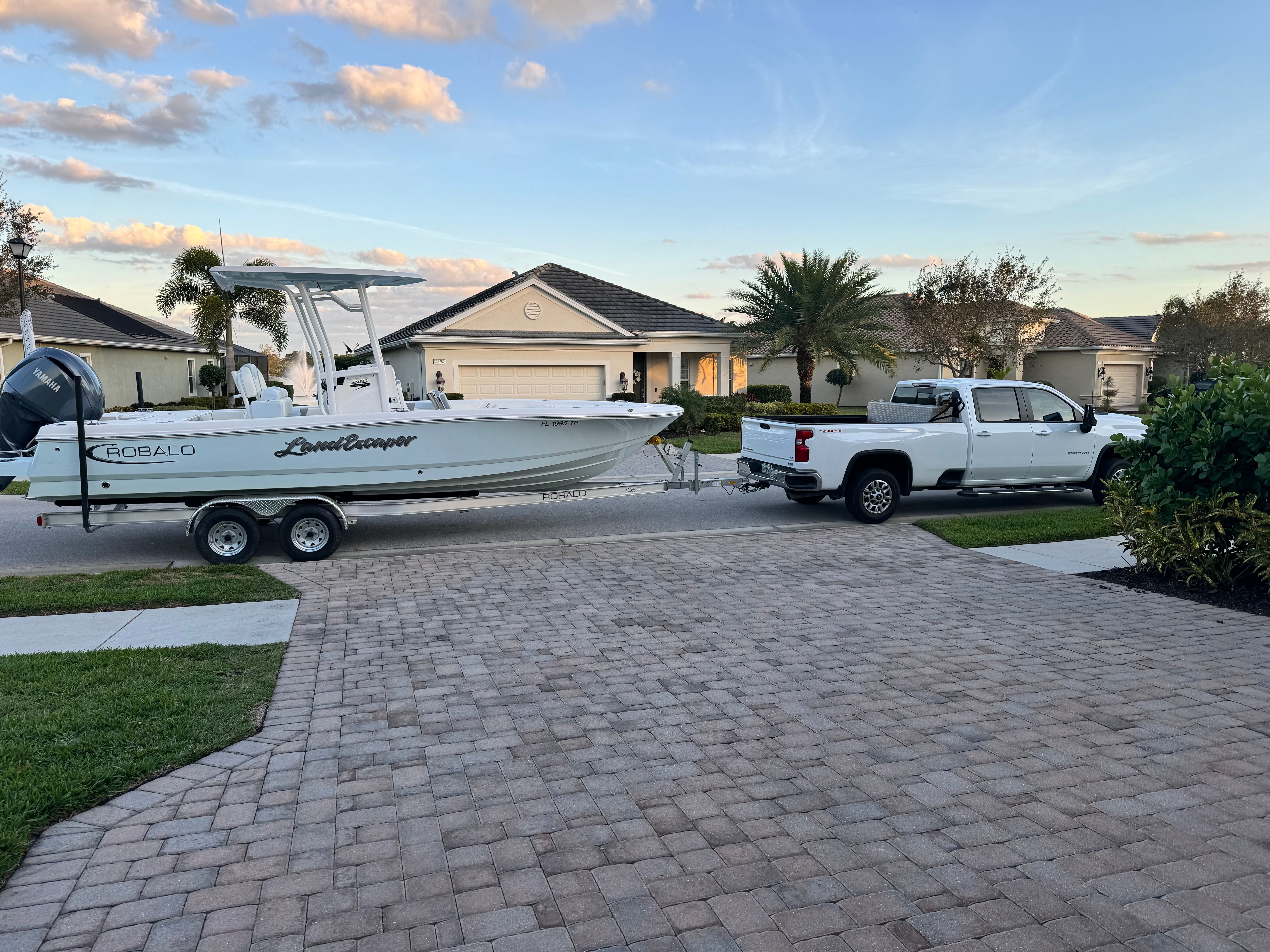 A Robalo 246 Cayman SD boat on a trailer, towed by a white pickup truck in a residential area.