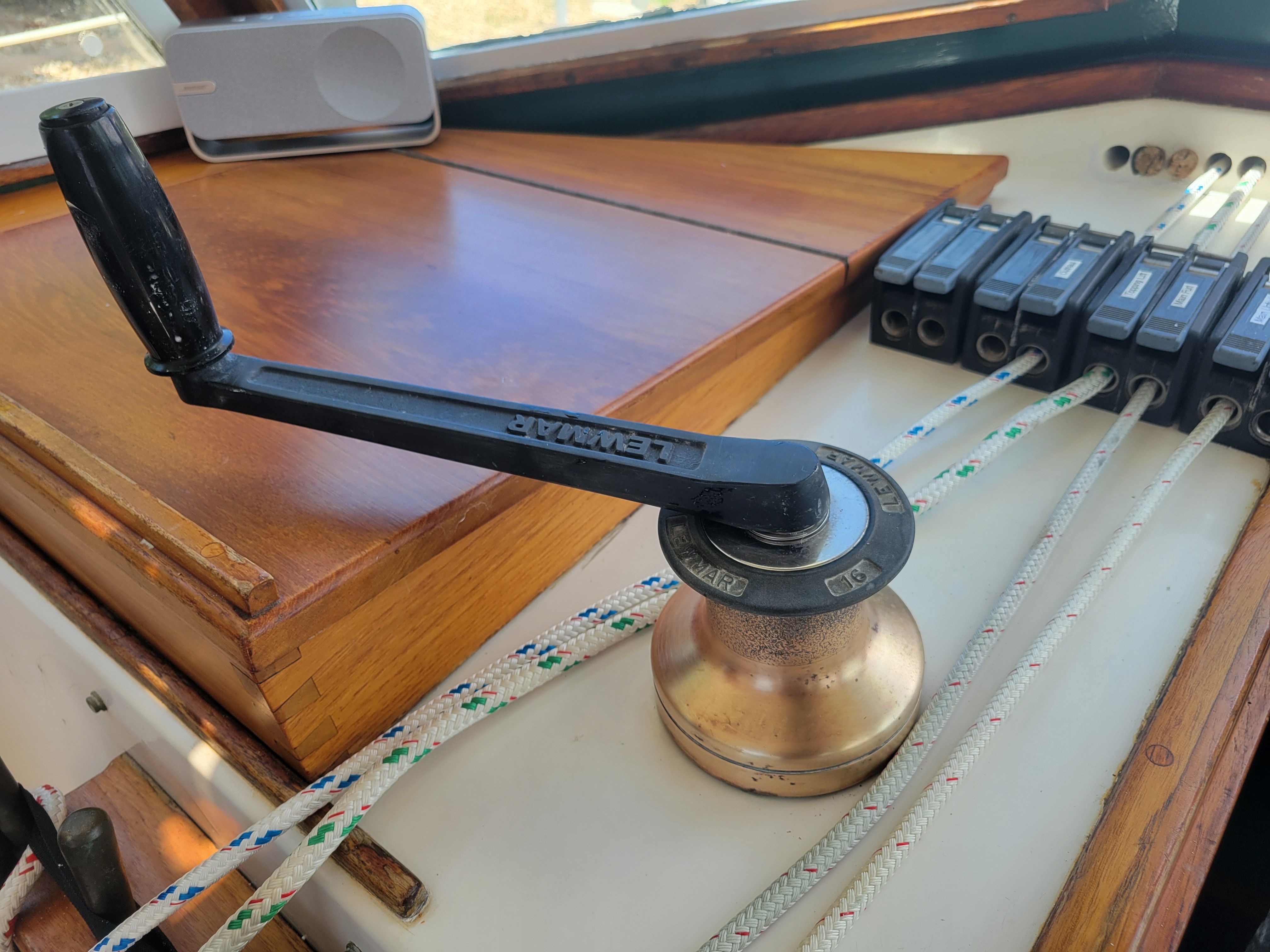 A winch with a handle on a sailboat, surrounded by several ropes.