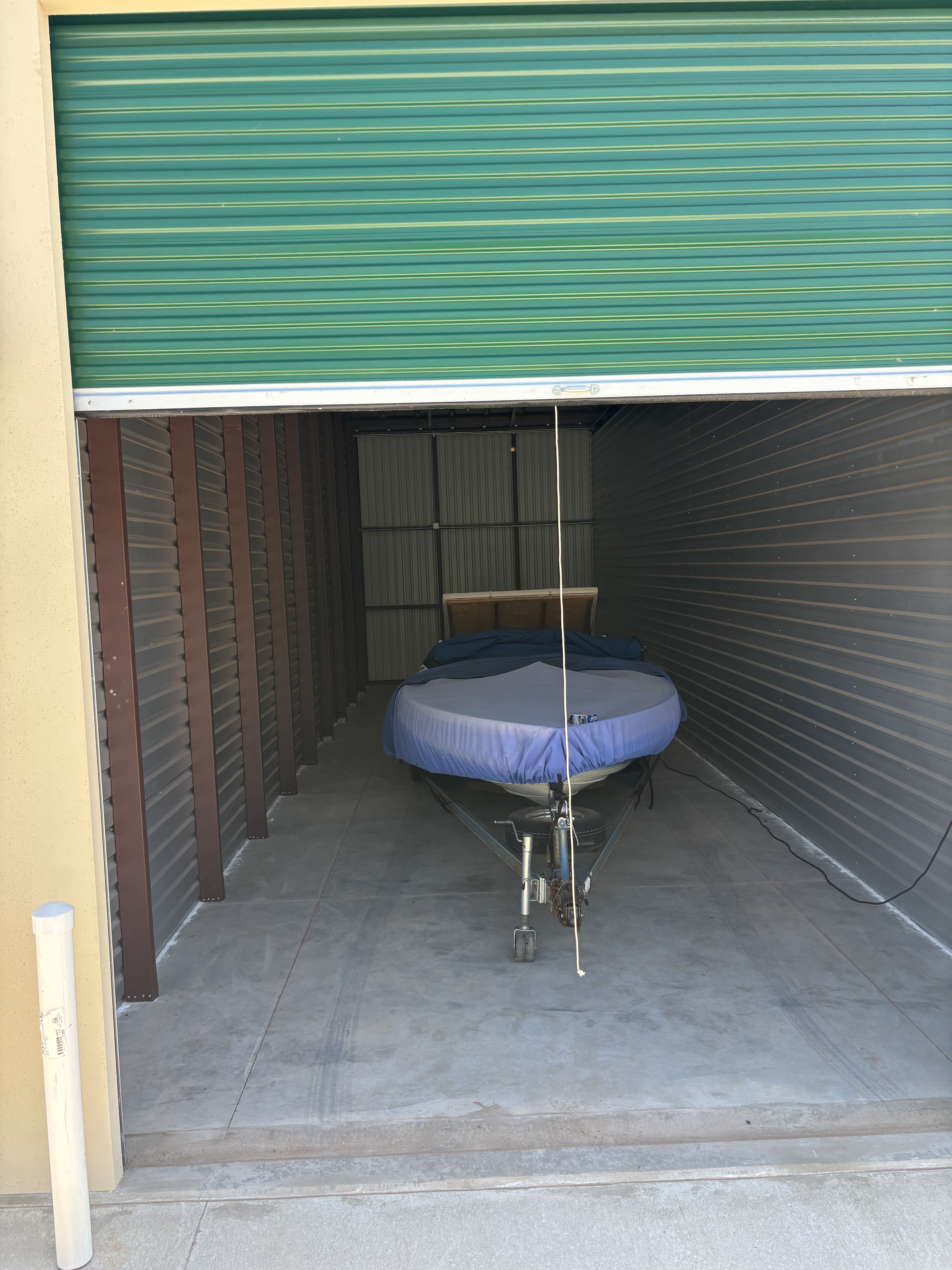A boat with a cover is stored in a unit with a partially open green door.