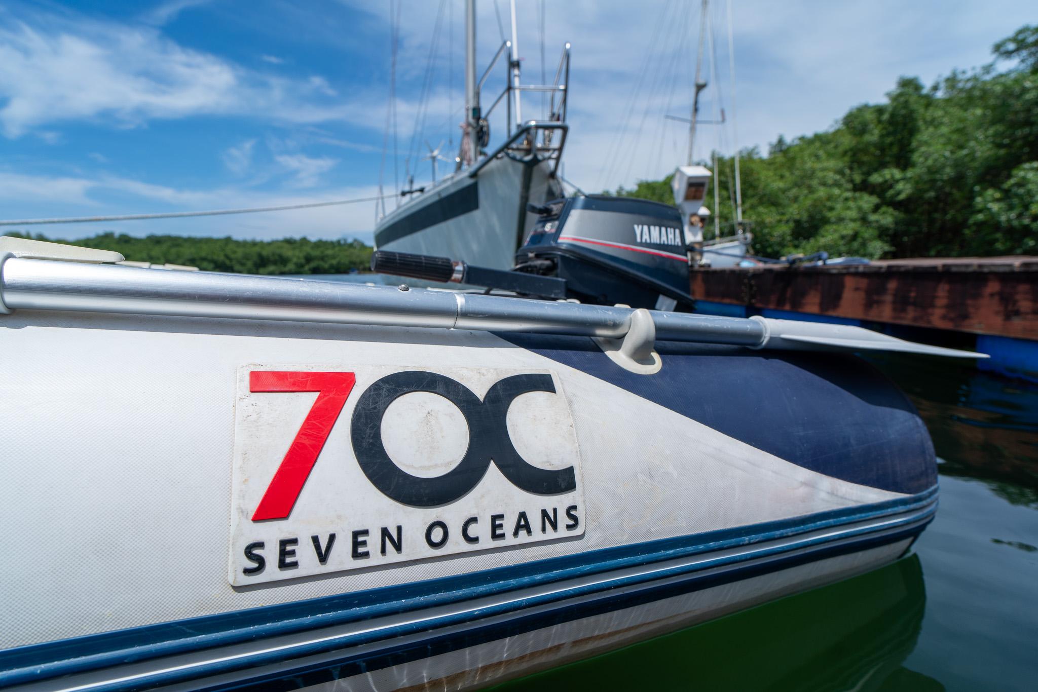 Inflatable boat with "Seven Oceans" logo, docked near other vessels, under a clear blue sky.