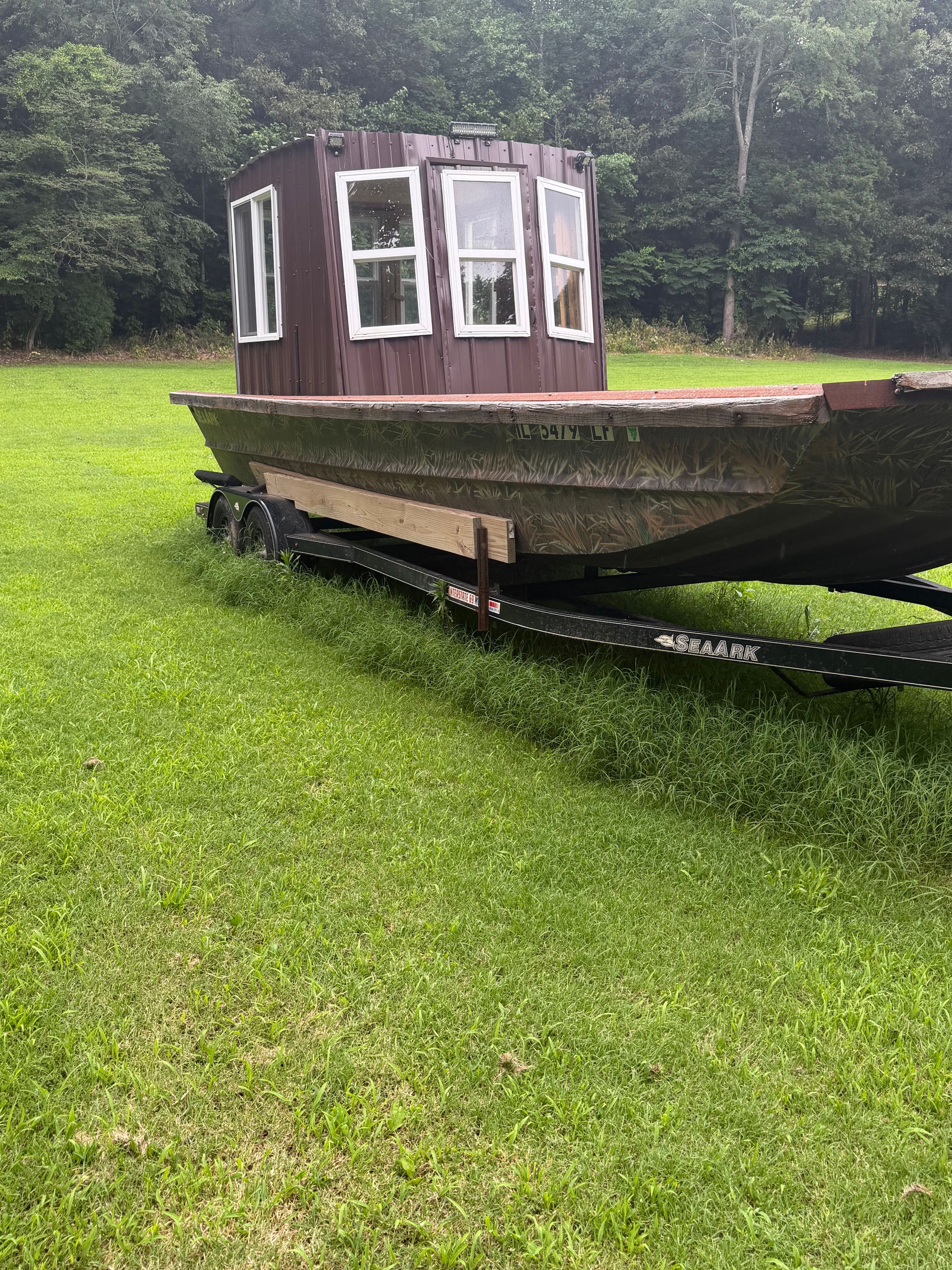 A 24-foot SeaArk boat with a wooden cabin sits on a trailer in a grassy area.