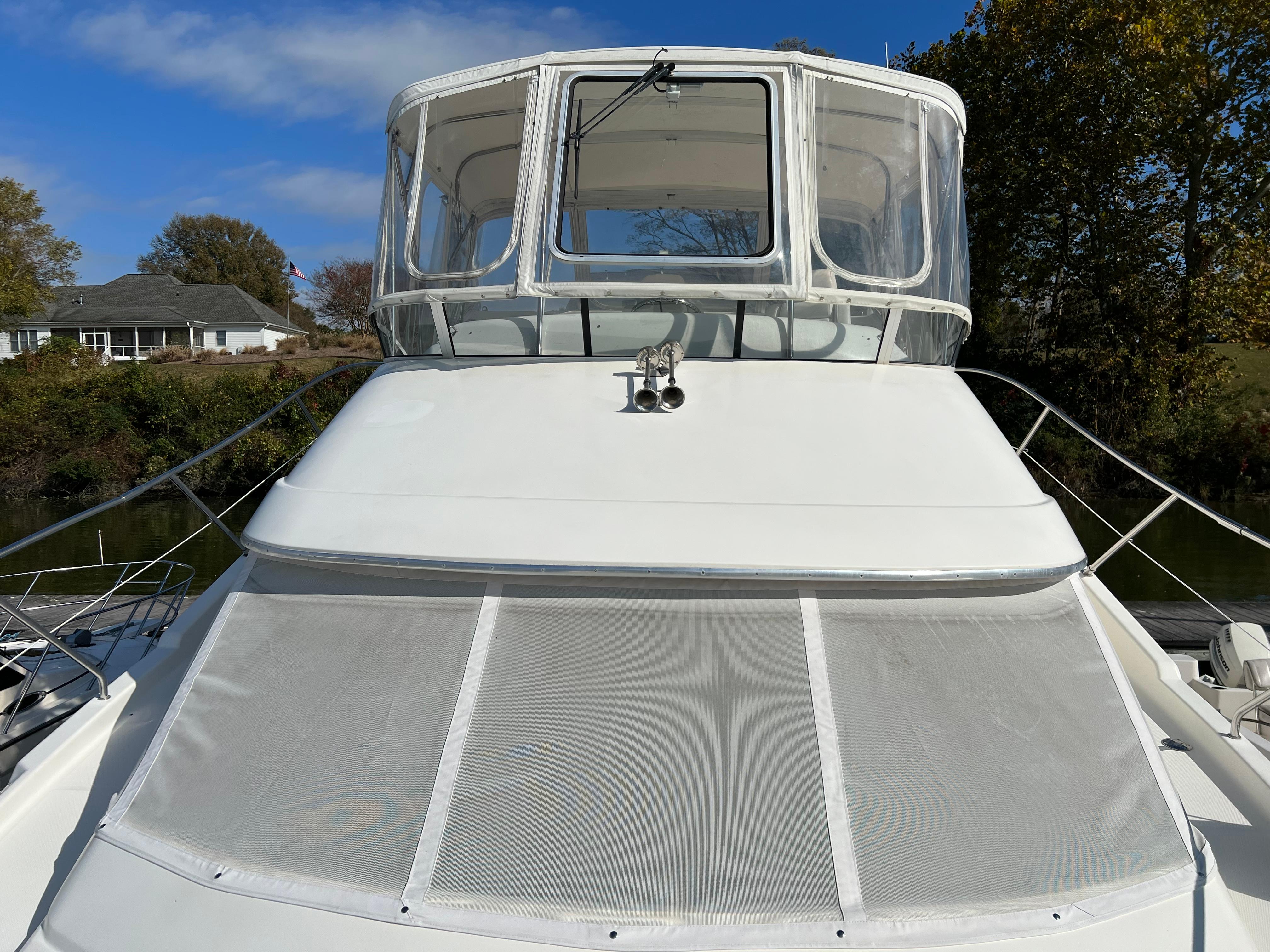 2004 Silverton 39 Motor Yacht with enclosed flybridge, docked near trees and houses.
