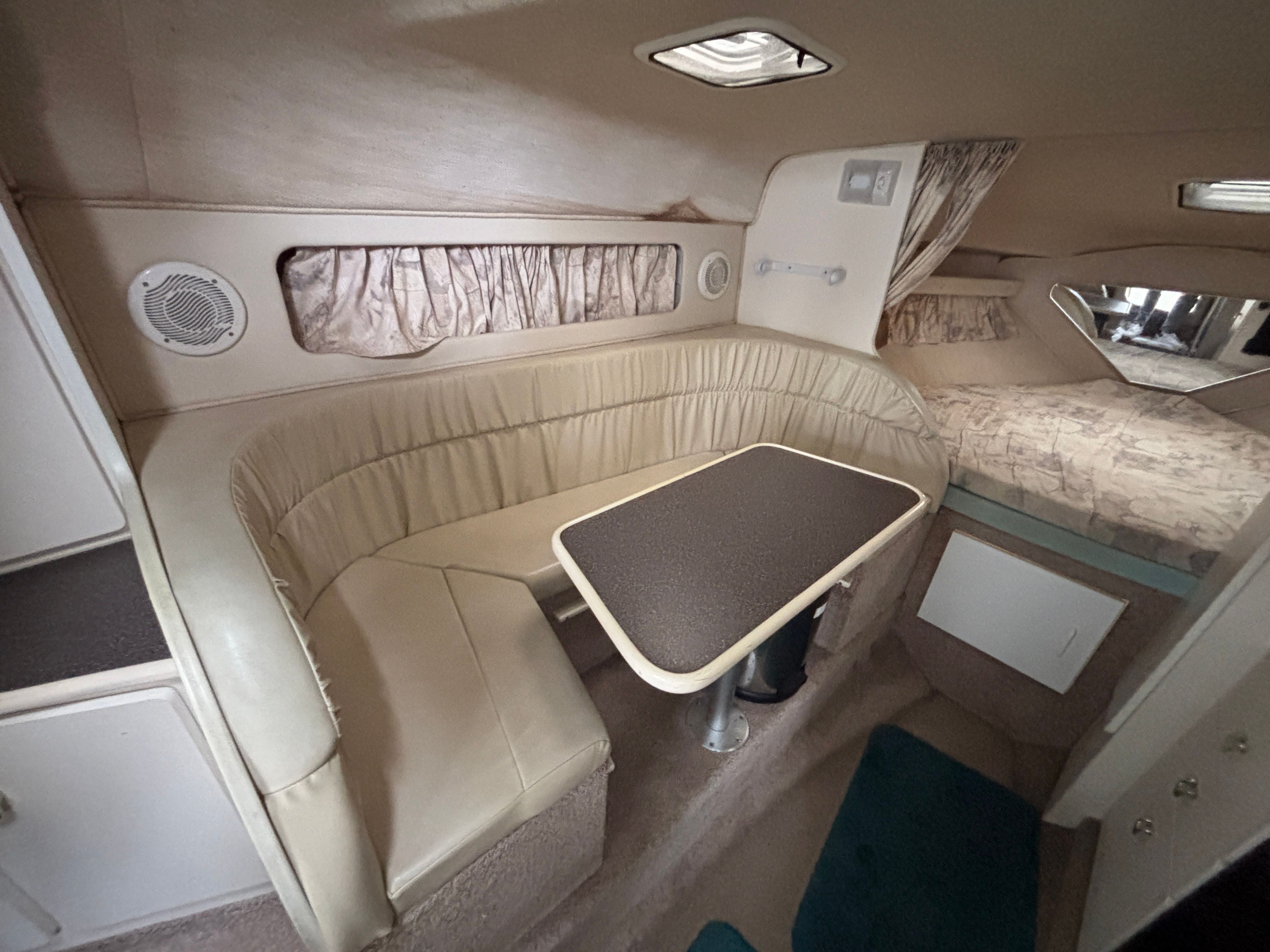 Interior of a yacht with beige sofa and table, sleeping area in the background.